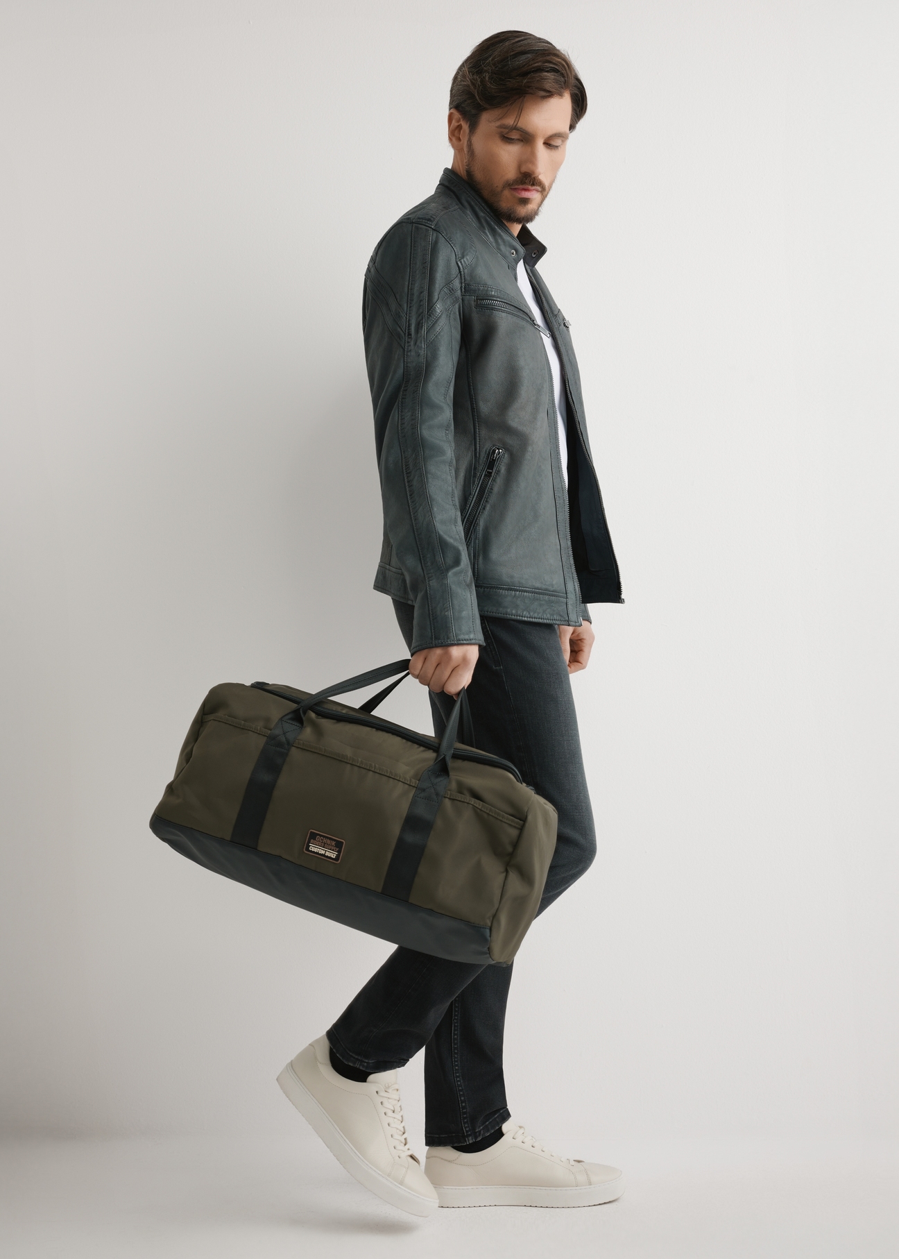 Torba podróżna w kolorze khaki TORMN-0417-8D(W26) - widok produktu z przodu, trzymanego przez modela w ręku, na jasnym tle. 