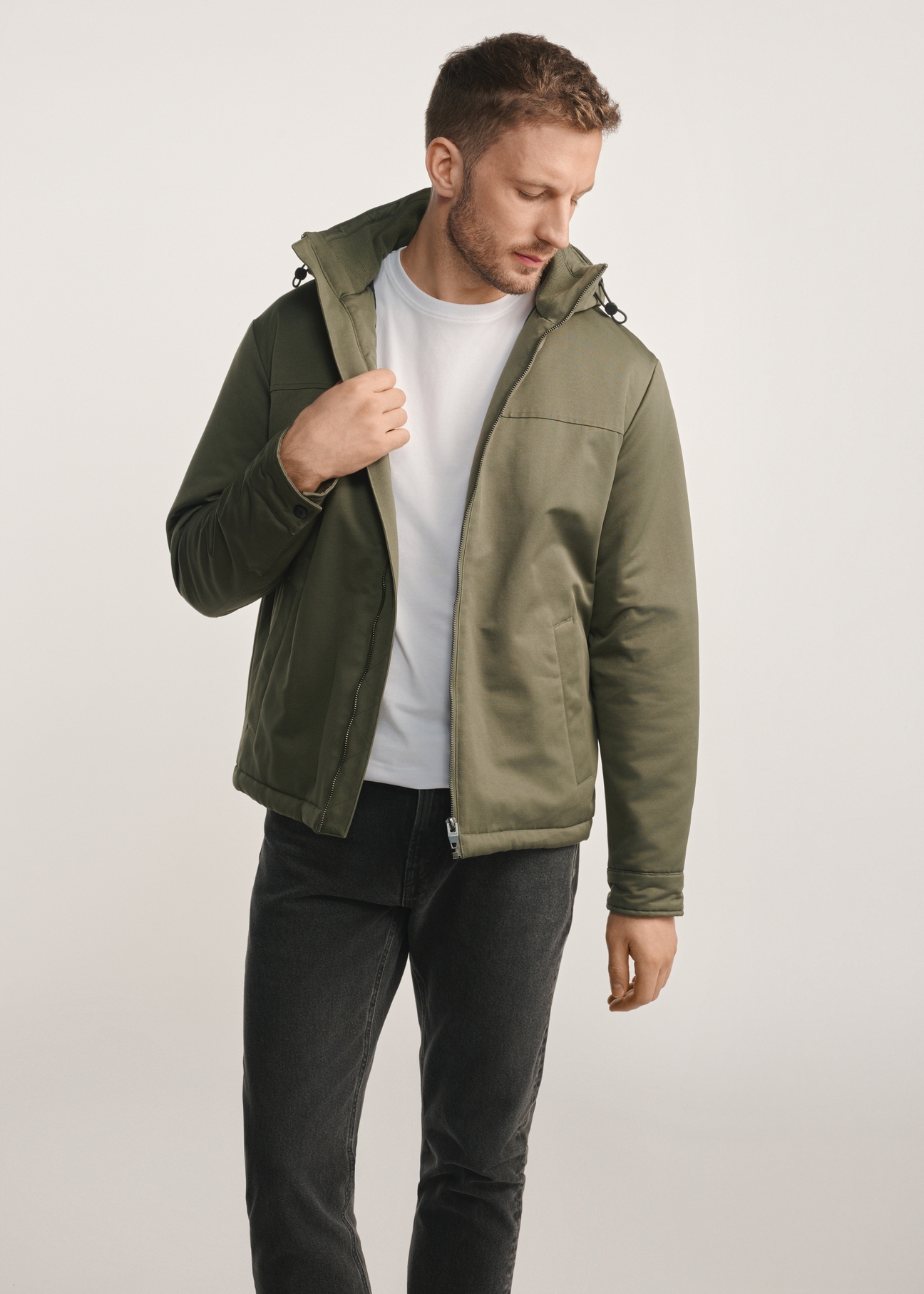 Kurtka męska w kolorze khaki KURMT-0386-54(Z25) - widok produktu z przodu na modelu na białym tle. Widoczna sylwetka do kolan. 