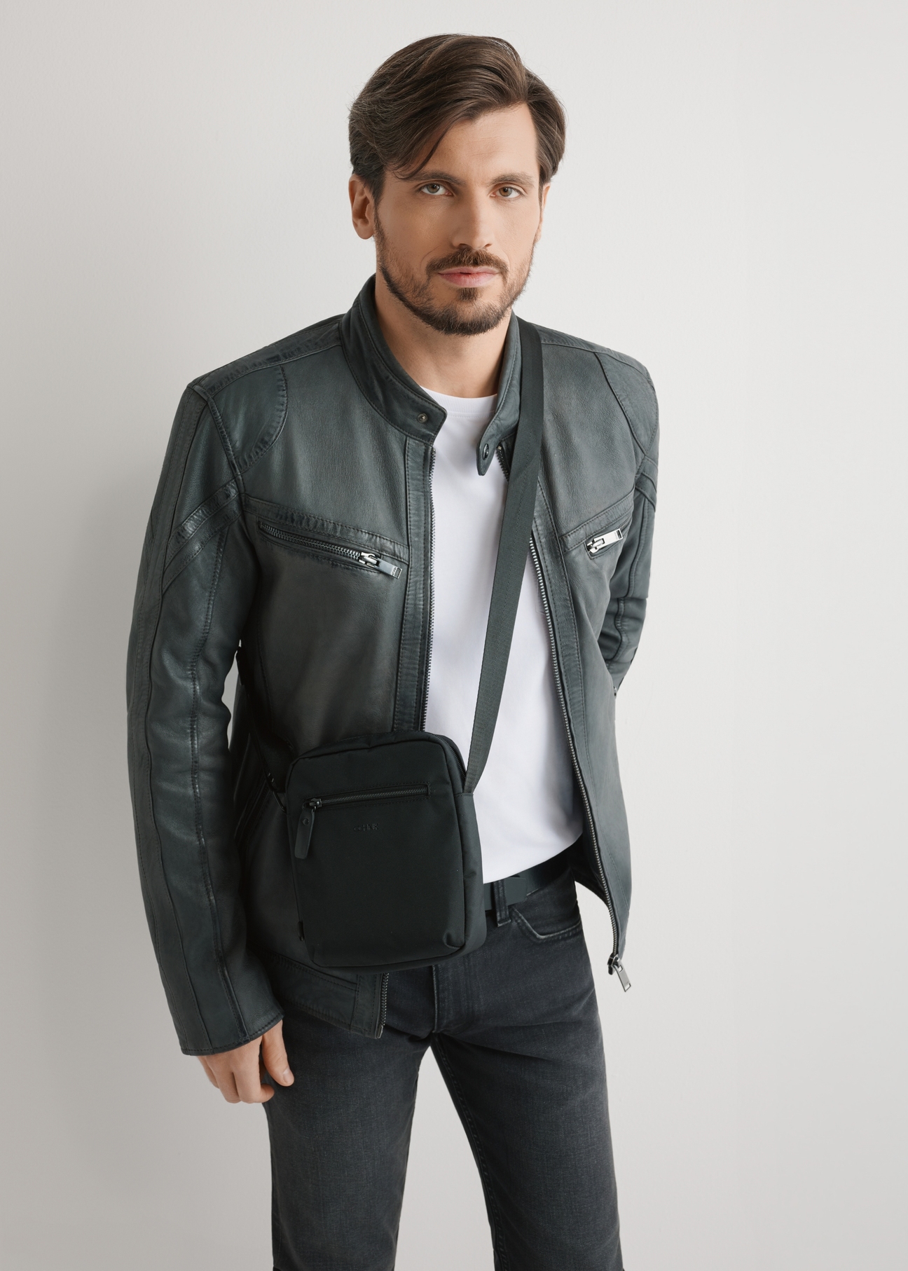 Czarna saszetka męska na ramię TORMN-0391-99(W26) - widok produktu z przodu, na modelu, na jasnym tle. Widoczna sylwetka do kolan.