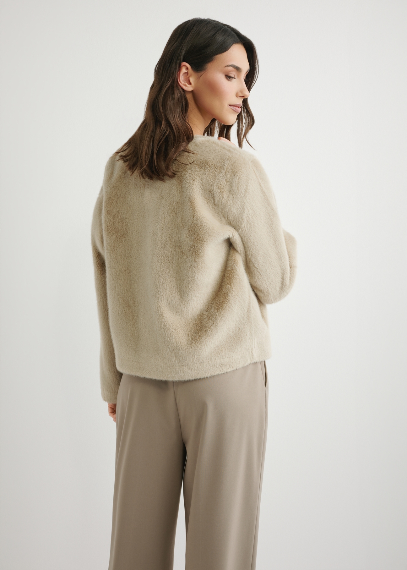 Krótkie beżowe futro damskie FUTDP-0079-1A(W26), widok produktu z tyłu na modelce. Widoczna połowa sylwetki.