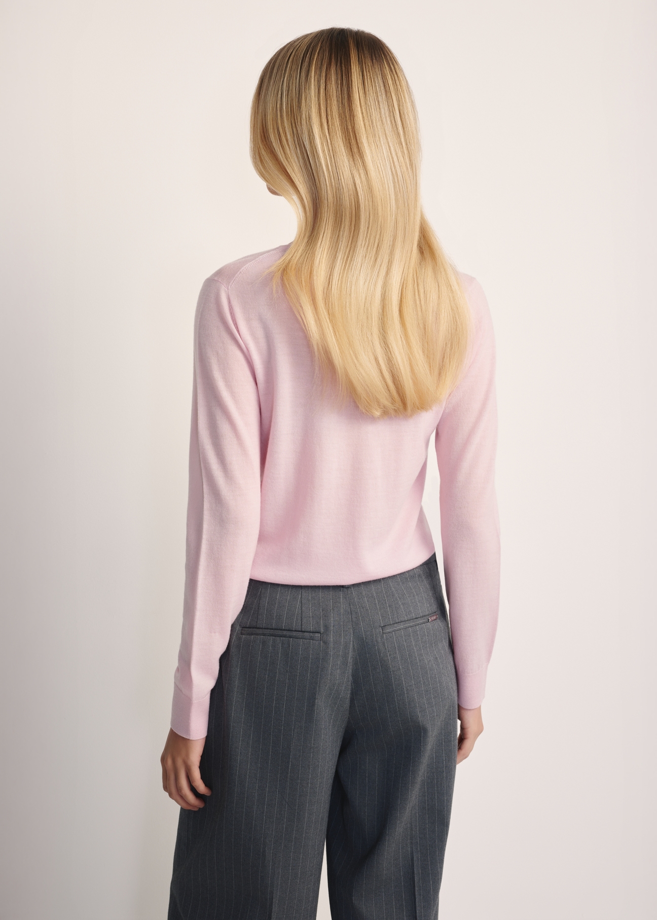 Jasnoróżowy sweter damski SWEDT-0250-34(Z25), widok produktu z tyłu na modelce. Widoczna połowa sylwetki.