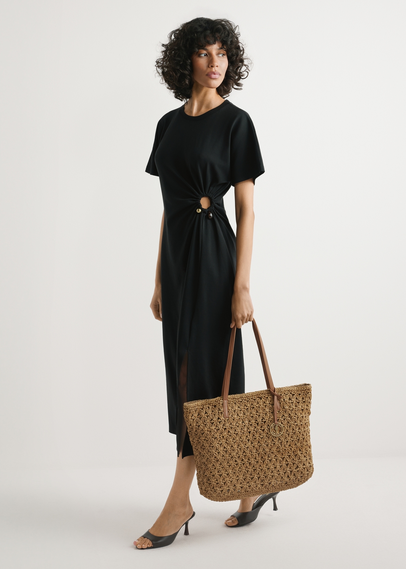 Słomkowa torebka shopper TOREC-1218-1E(W26) - widok produktu lekko po skosie, trzymanego przez modelkę w ręku, na jasnym tle. Widoczna cała sylwetka. 