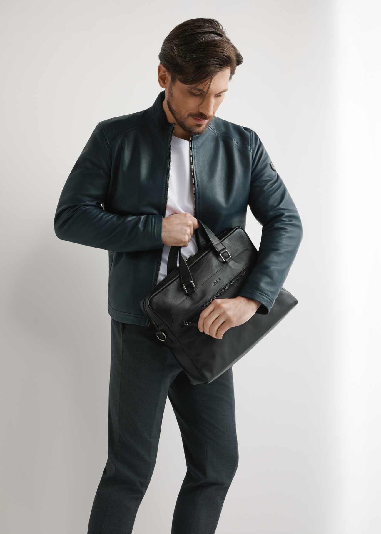 Czarna skórzana torba na laptopa TORMS-0496-99(W26) - widok produktu po skosie, trzymanego przez modela w ręku, na jasnym tle. Widoczna cała sylwetka. 