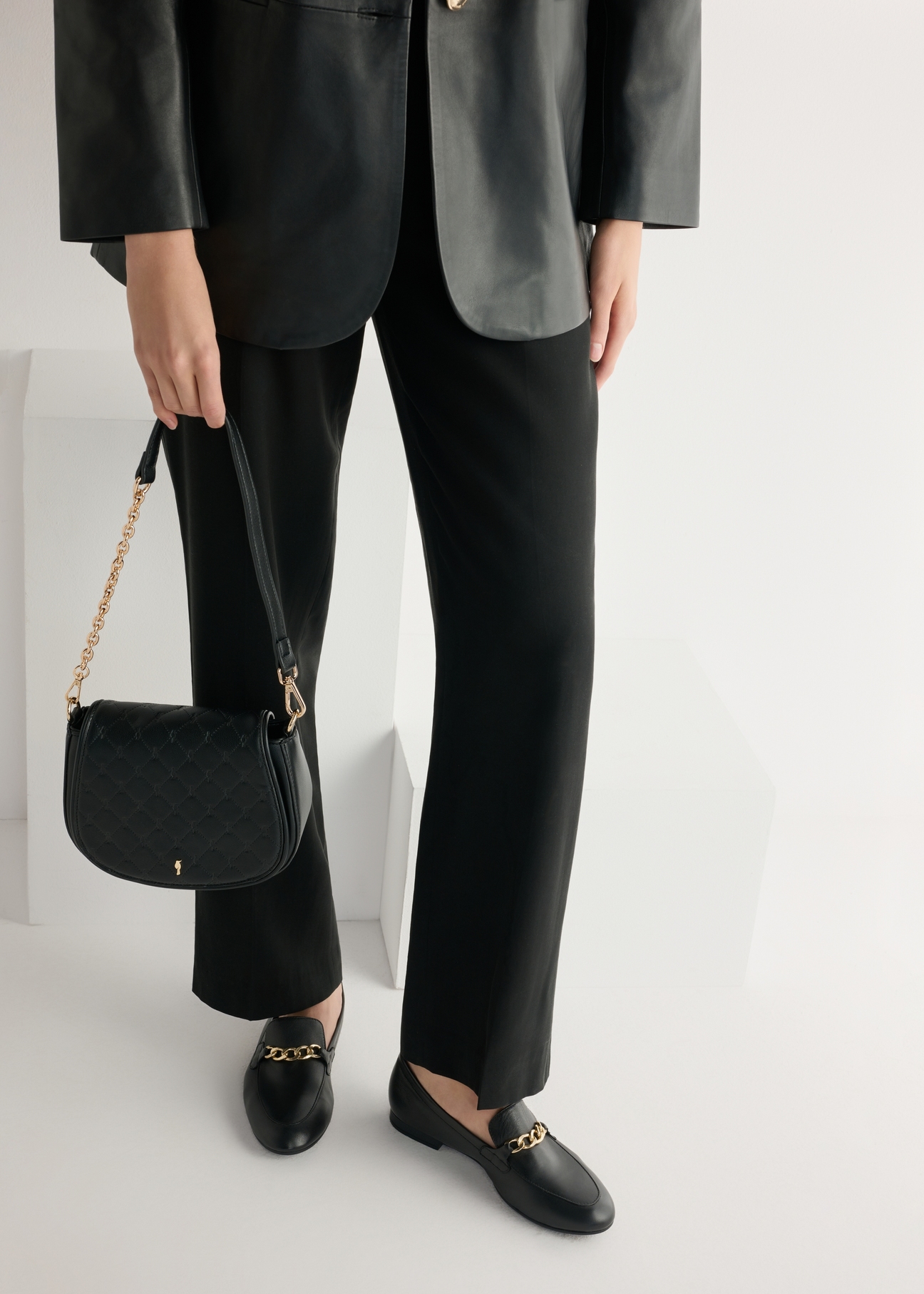 Skórzane czarne mokasyny damskie z łańcuszkiem BUTYD-0914A-99(W26), widok produktu od boku na modelce, widoczna połowa sylwetki.