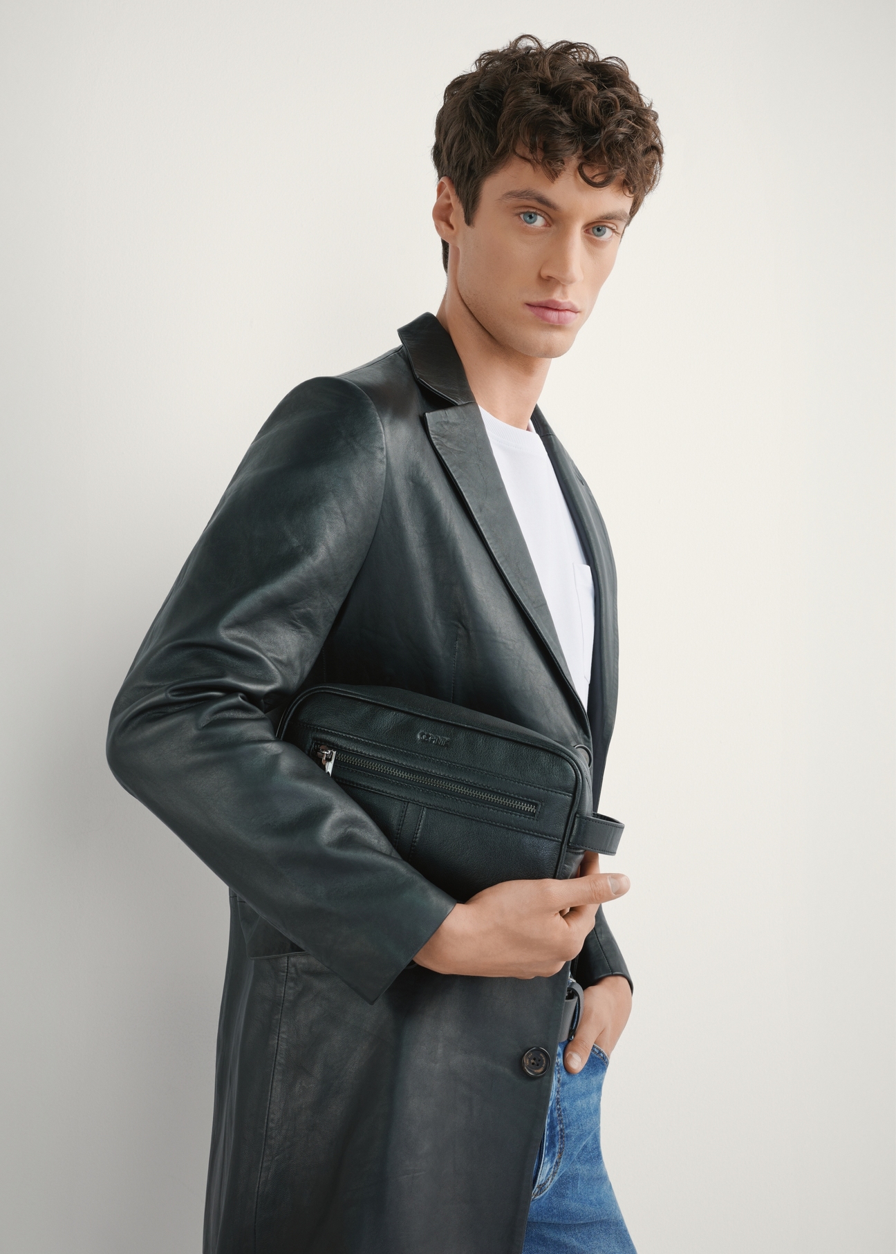 Czarna skórzana kosmetyczka męska TORMS-0490-99(W26) - widok produktu, trzymanego przez modela w ręku, na jasnym tle. Widoczna połowa sylwetki. 