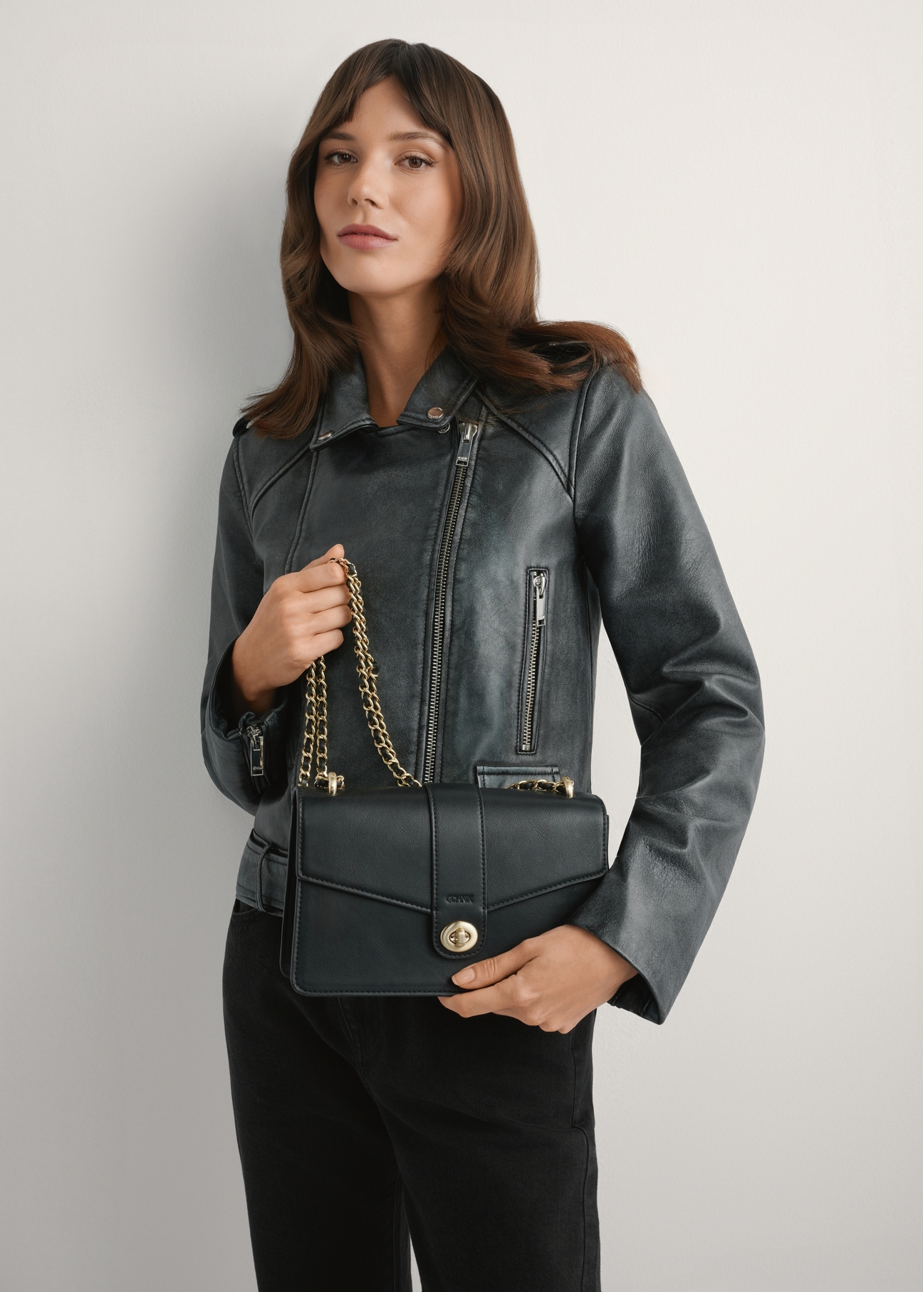 Czarna torebka listonoszka damska TOREC-1137-99(W26), widok produktu w rękach modelki. Widoczna połowa sylwetki.