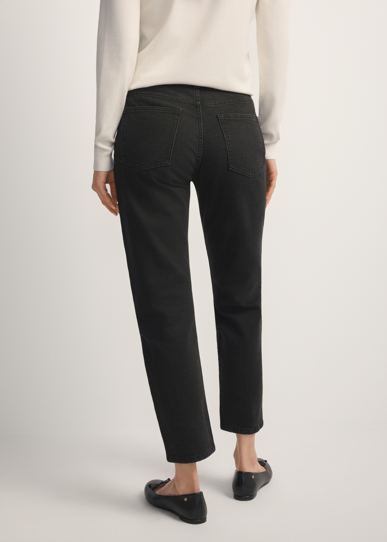 Czarne spodnie jeansowe damskie JEADT-0011-99(W26), widok produktu z tyłu na modelce. Widoczna połowa sylwetki.