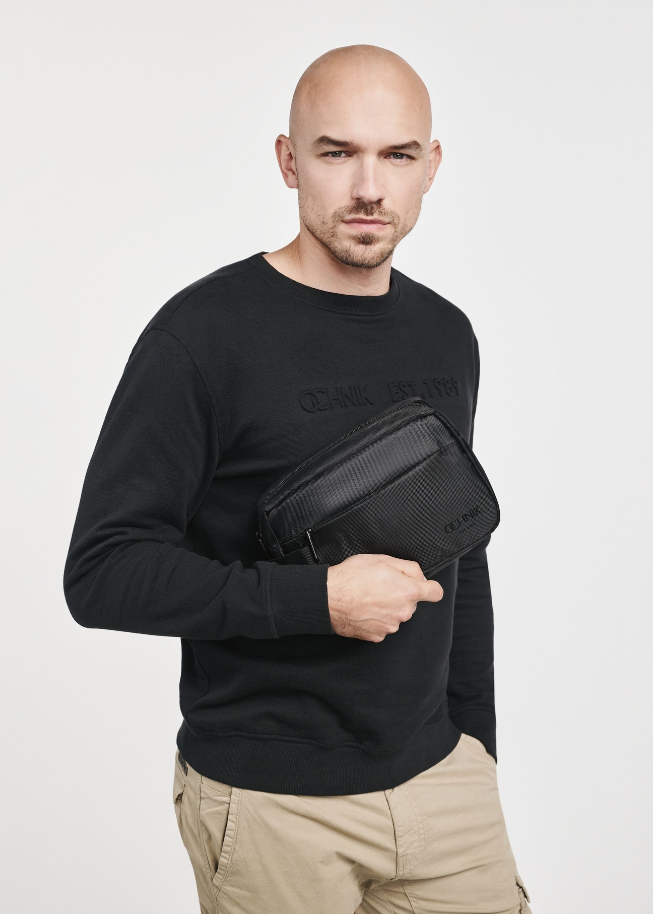 Czarna kosmetyczka męska TORMS-0267C-99(Z25), zbliżenie na produkt w dłoni modela. Widoczna połowa sylwetki.