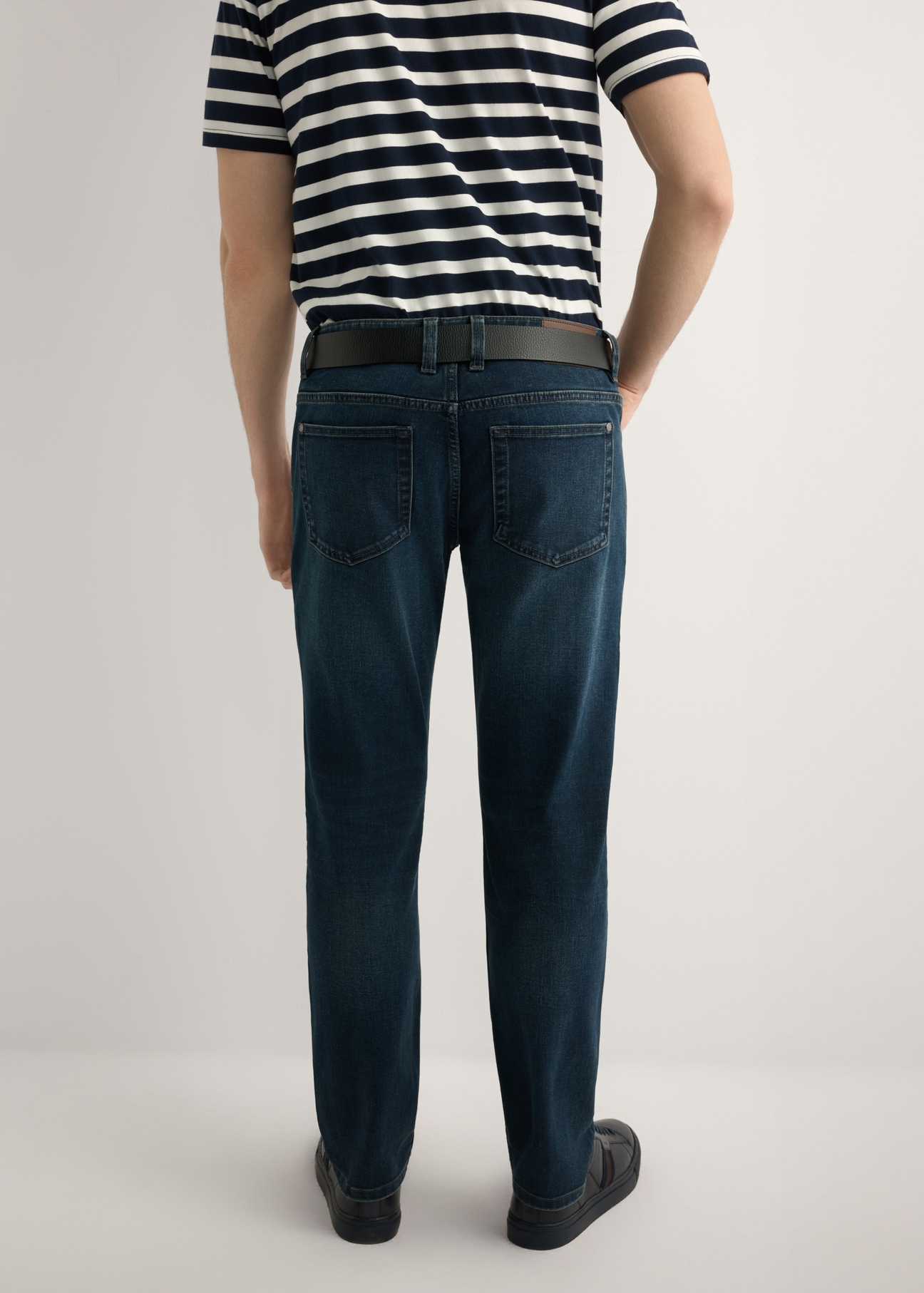 Ciemnoniebieskie jeansowe spodnie męskie JEAMT-0022-7C(W26), widok produktu z tyłu na modelu. Widoczna połowa sylwetki.