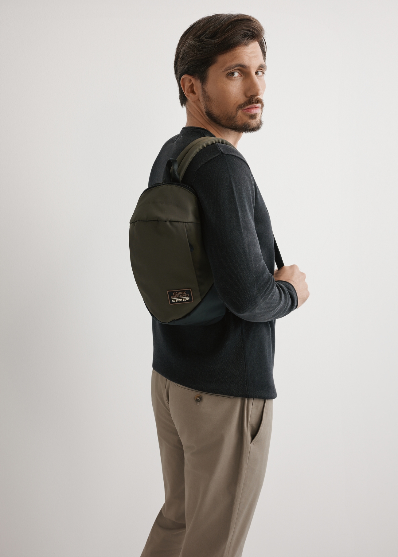 Męska torba na ramię w kolorze khaki TORMN-0416-8D(W26) - widok produktu lekko po skosie, na jasnym tle. Widoczna sylwetka do kolan.