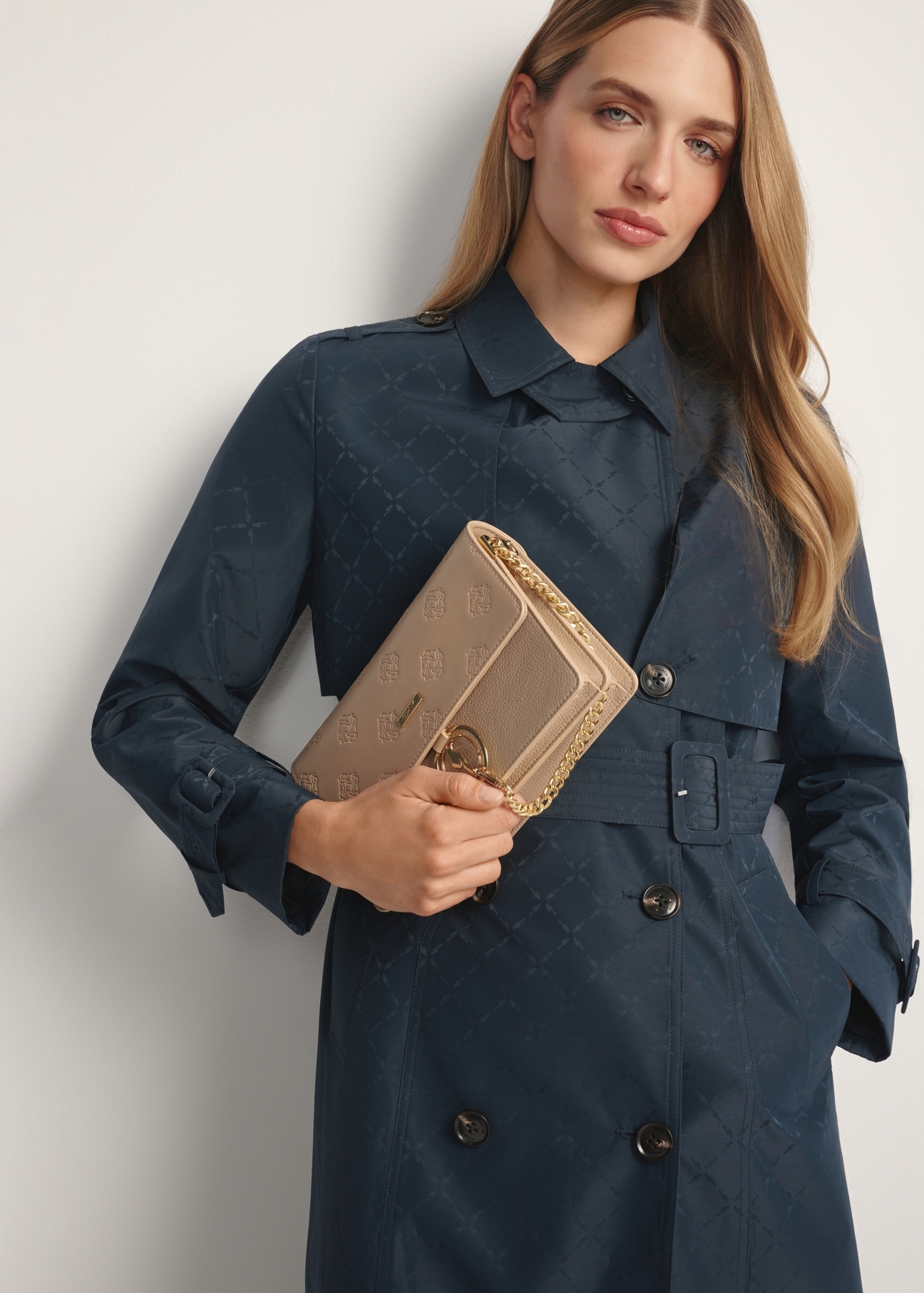 Beżowa torebka damska z monogramem TOREC-0536-1P(W26), widok produktu w dłoni modelki. Widoczna połowa sylwetki.