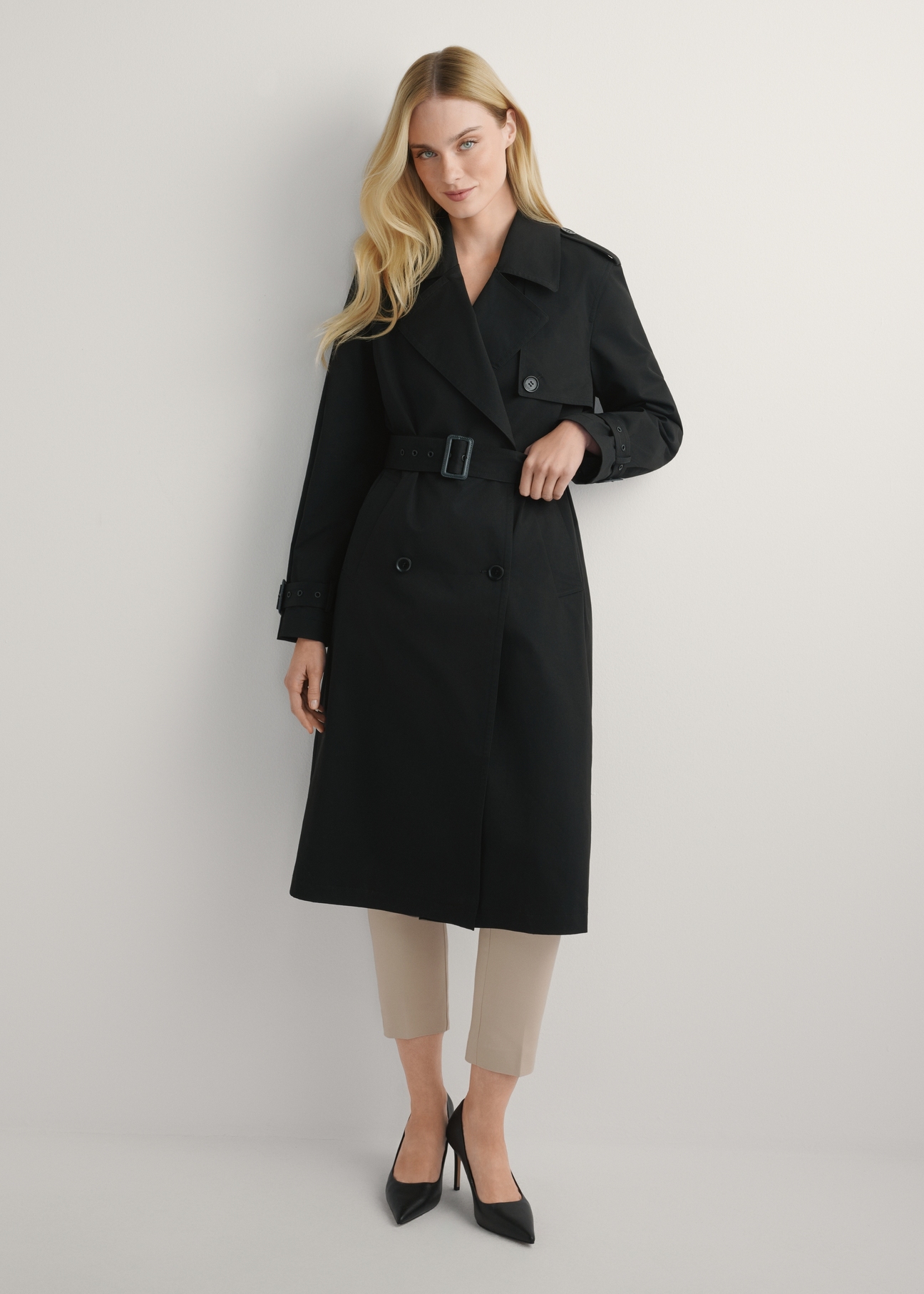 Długa czarna kurtka damska w formie płaszcza KURDT-0512-99(W25), widok produktu od przodu na modelce, widoczna cała sylwetka.