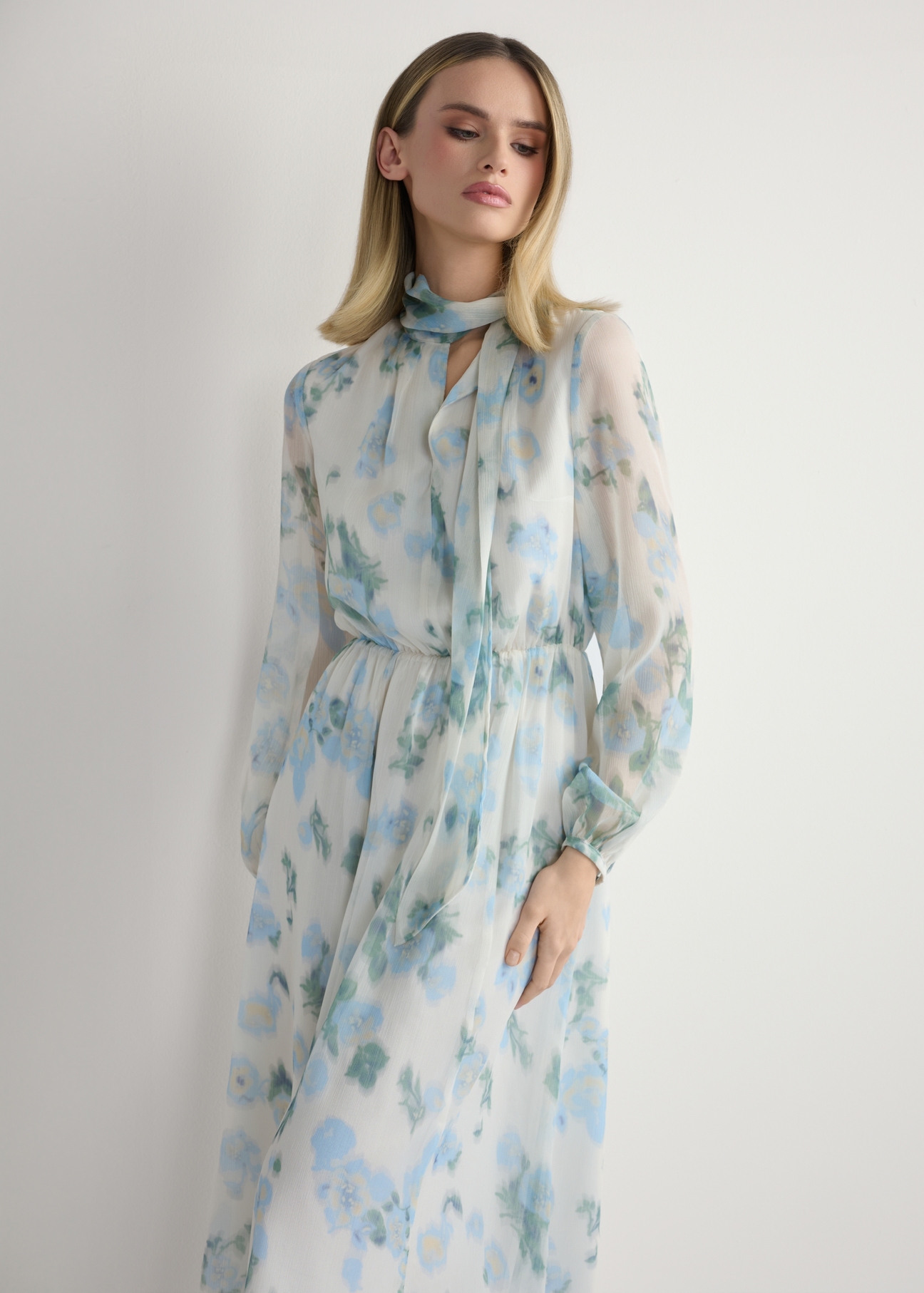 Kremowa sukienka damska w kwiaty SUKDT-0265-7P(W26), widok produktu z przodu na modelce. Widoczna połowa sylwetki.