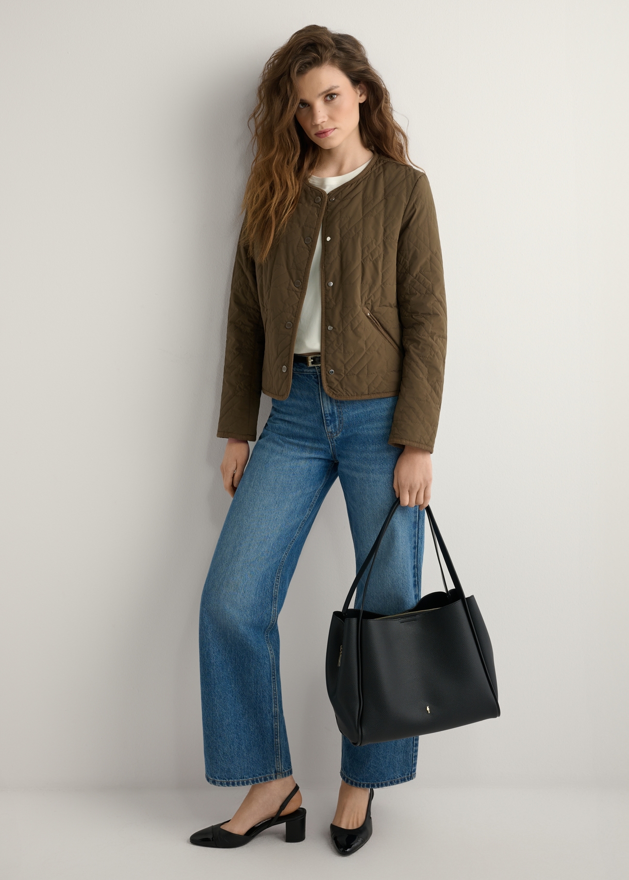 Czarna torebka shopper damska TOREC-1183-99(W26) - widok produktu lekko po skosie, trzymanego przez modelkę w ręku, na jasnym tle. Widoczna cała sylwetka. 