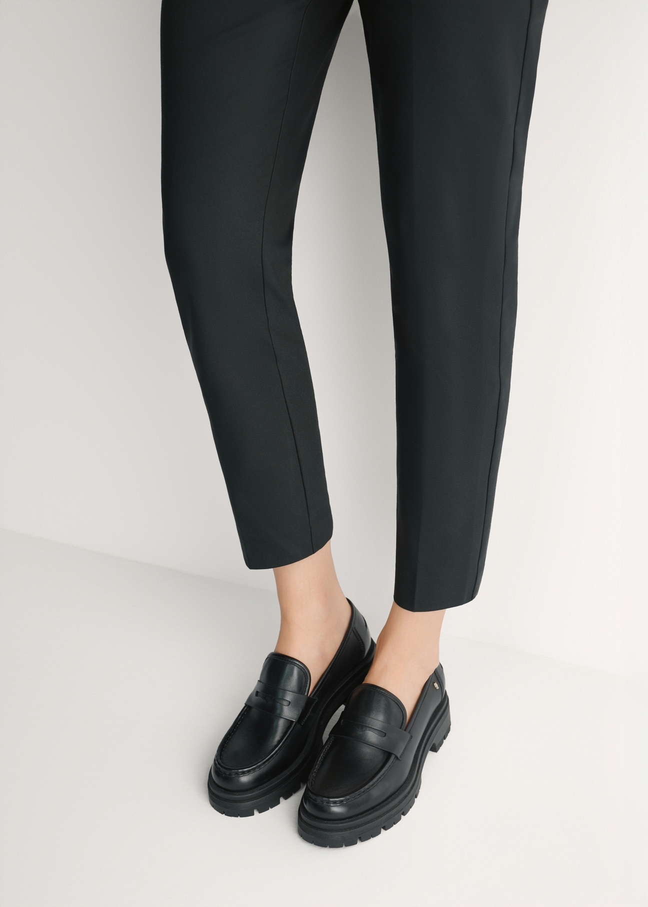 Czarne skórzane loafersy damskie BUTYD-1069-99(W26) - widok produktu z przodu, na modelce, na jasnym tle. Widoczna sylwetka do kolan. 