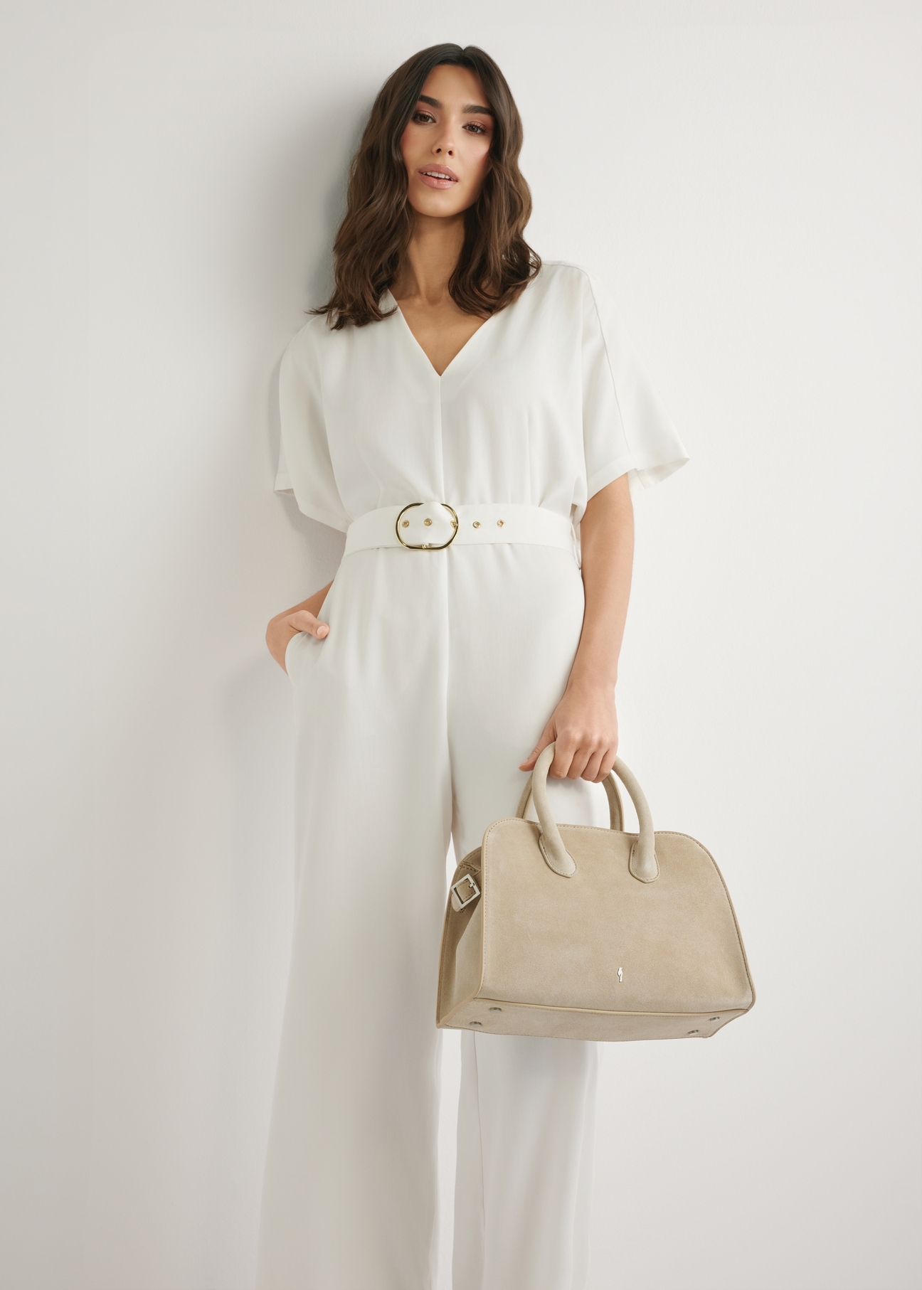 Kremowa zamszowa torebka damska TORES-1295-0B(W26), widok produktu w dłoni modelki. Widoczna połowa sylwetki.