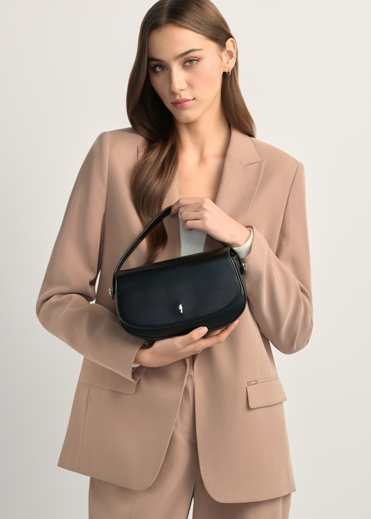 Mała czarna torebka listonoszka damska TOREC-1185-99(W26), widok produktu w rękach modelki. Widoczna połowa sylwetki.