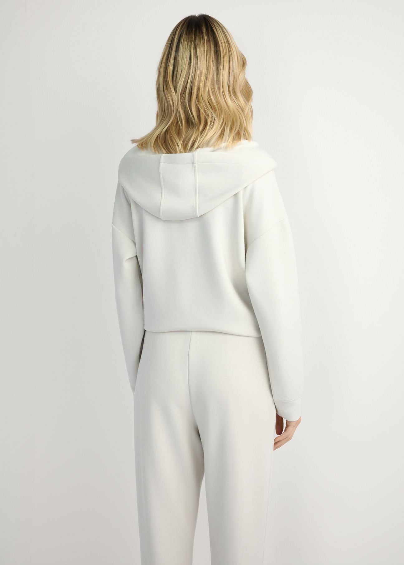 Jasnobeżowa bluza damska z kapturem BLZDT-0111A-1A(W26), widok produktu z tyłu na modelce. Widoczna połowa sylwetki.