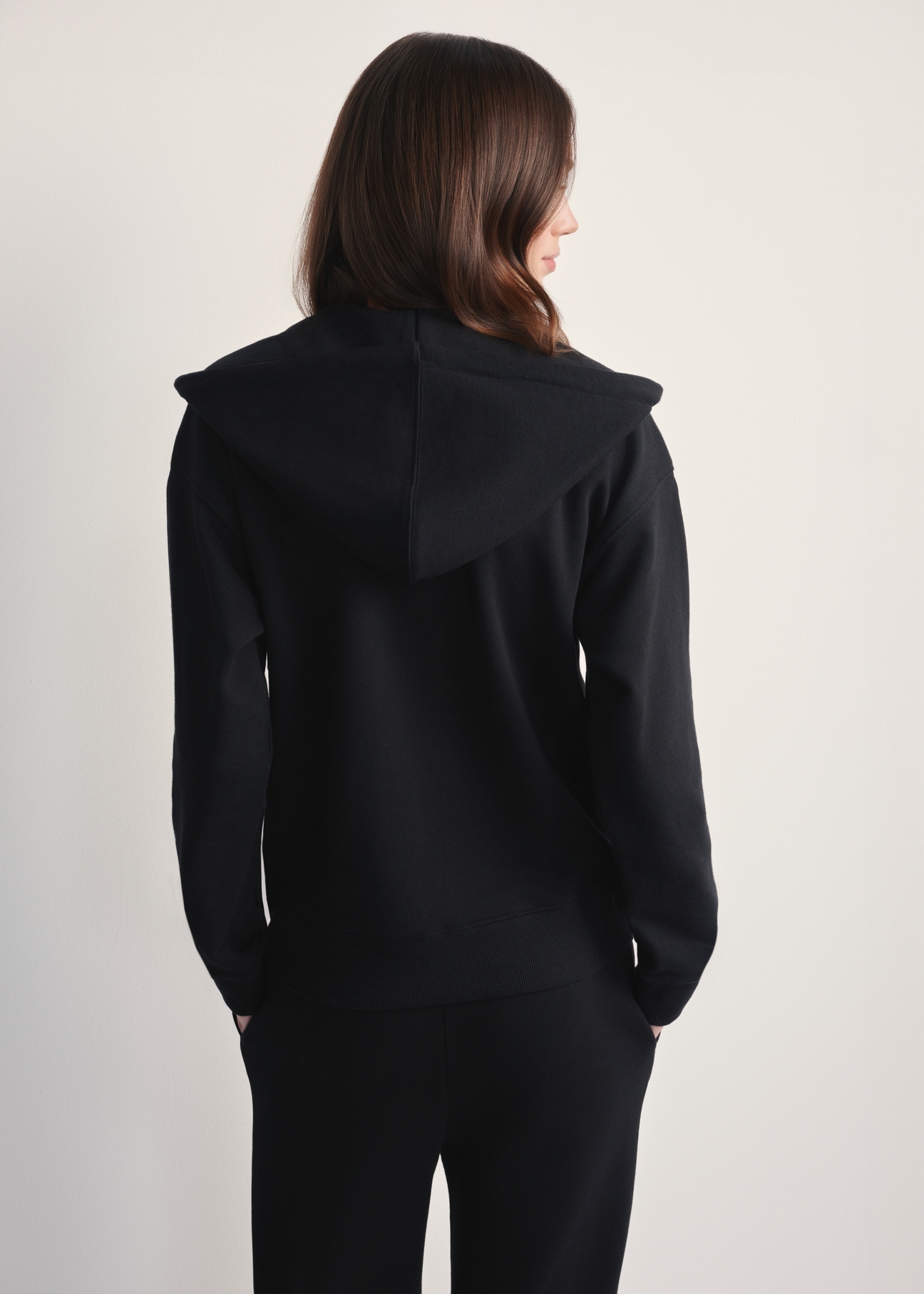Czarna bluza damska z kapturem BLZDT-0115-99(Z25), widok tyłu na modelce na jasnym tle. Widoczna połowa sylwetki. 