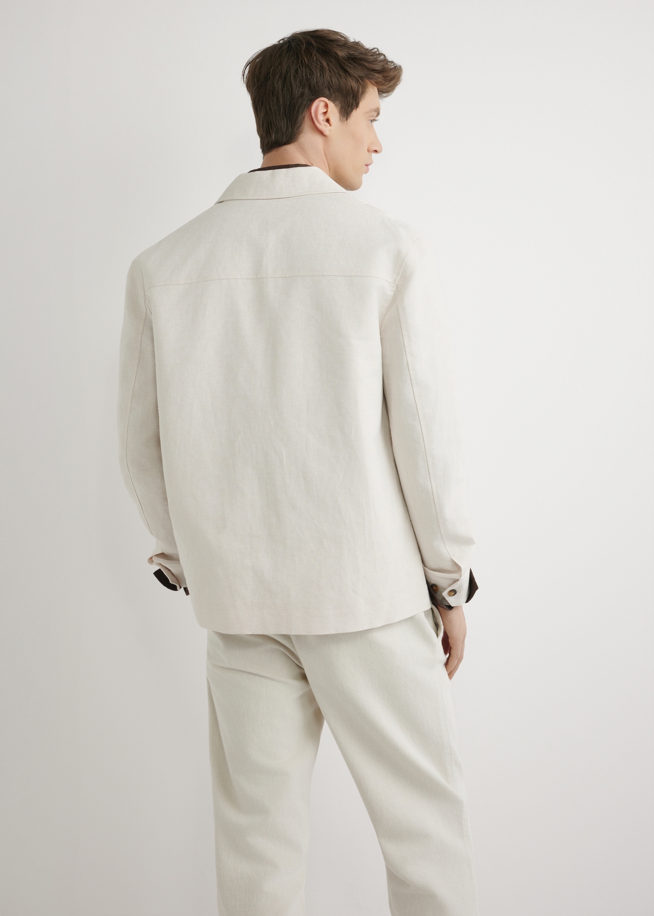 Jasnobeżowa lniana kurtka męska KURMT-0420-1A(W26) - widok produktu z tyłu, na modelu, na jasnym tle. Widoczna połowa sylwetki. 