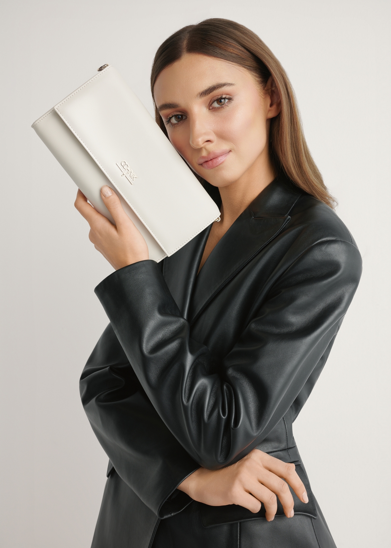 Kremowa torebka kopertówka TOREC-1210-0B(W26) - widok produktu trzymanego przez modelkę w ręku, na jasnym tle. Widczona połowa sylwetki. 