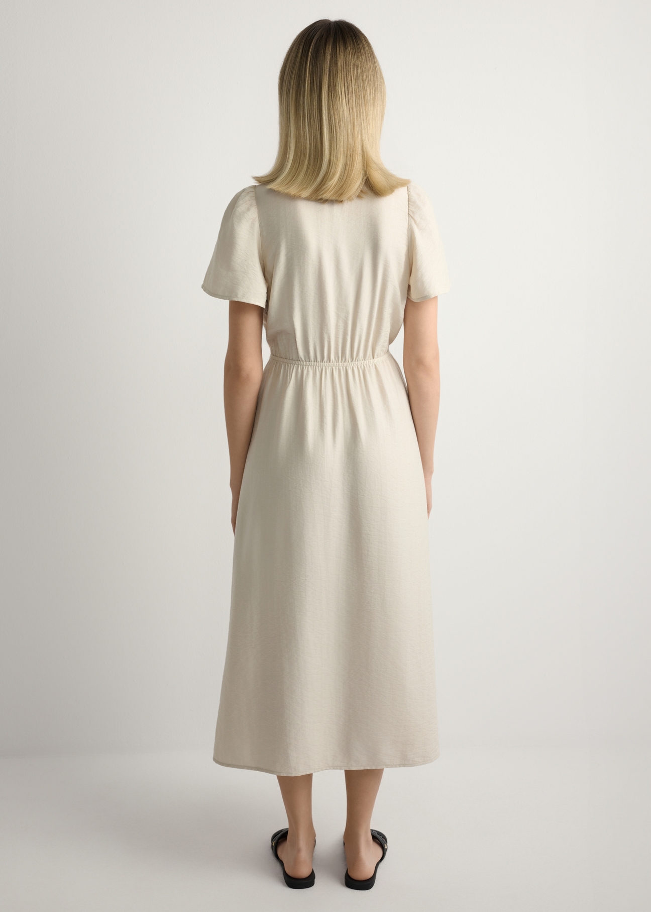 Sukienka damska w kolorze jasnego beżu SUKDT-0255-1A(W26), widok produktu z tyłu na modelce. Widoczna cała sylwetka.