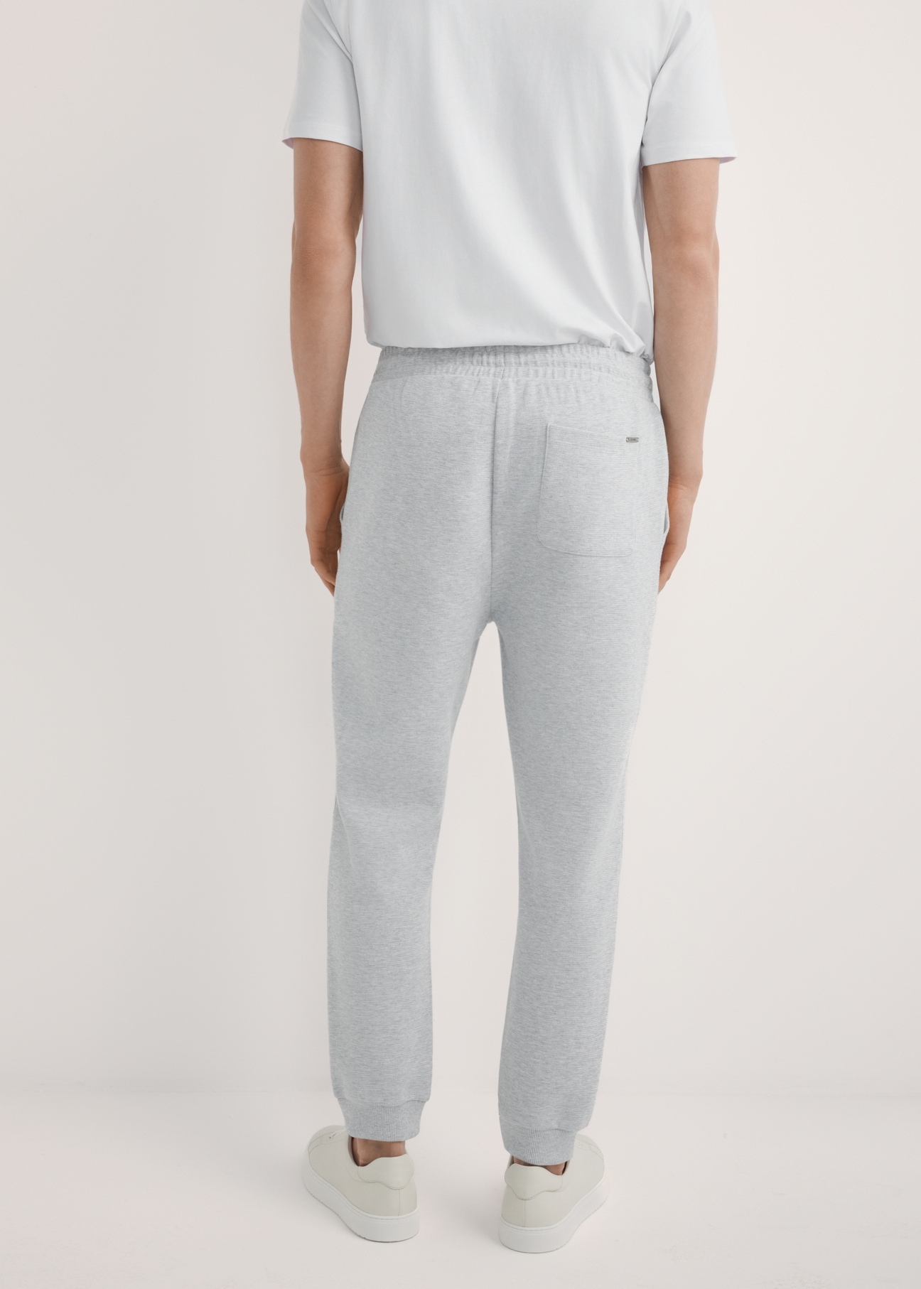 Szare dresowe spodnie męskie SPOMT-0116-9A(W26), widok produktu z tyłu na modelu. Widoczna połowa sylwetki.