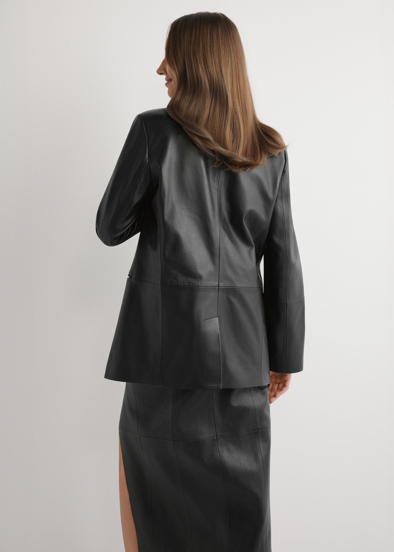 Czarna skórzana marynarka damska KURDS-0606-99(W26) - widok produktu z tyłu na modelu, na jasnym tle. Widoczna sylwetka do kolan.