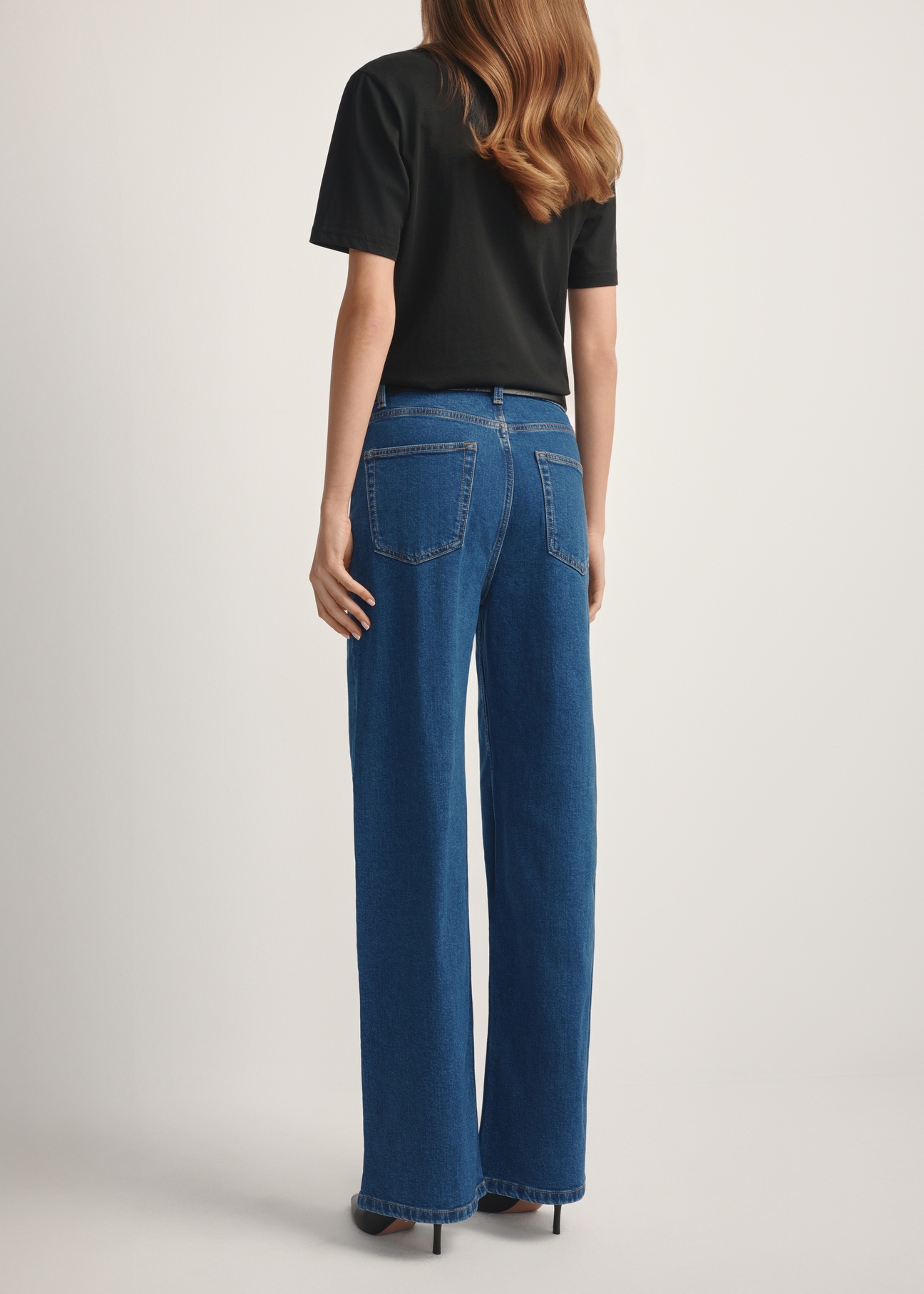 Niebieskie jeansowe spodnie damskie JEADT-0014-7H(W26), widok produktu z tyłu na modelce. Widoczna połowa sylwetki.