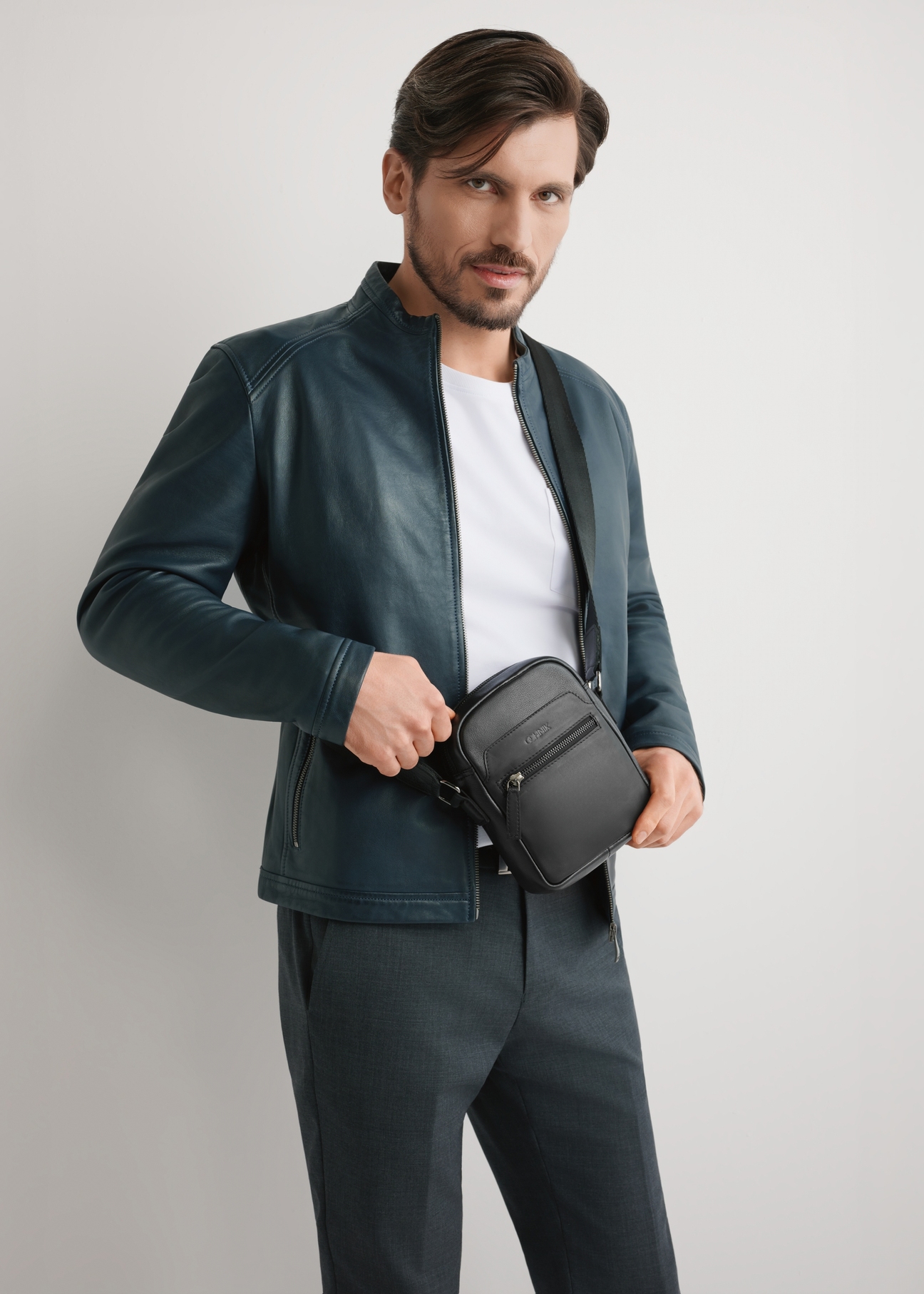 Czarna mała skórzana torba męska TORMS-0498-99(W26) - widok produktu z przodu, na modelu, na jasnym tle. Widoczna sylwetka do kolan. 