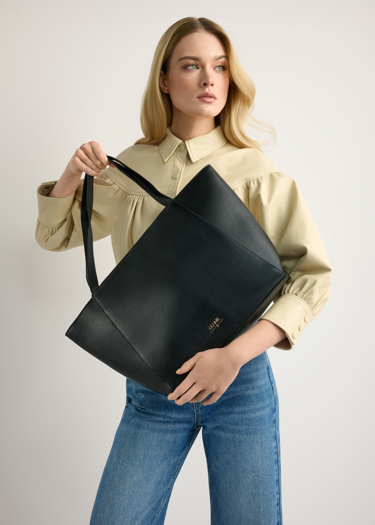 Czarna skórzana torebka shopper TORES-1209-9I(W26) - widok produktu z przodu, trzymanego przez modelkę w ręku, na jasnym tle. Widoczna sylwetka do kolan. 