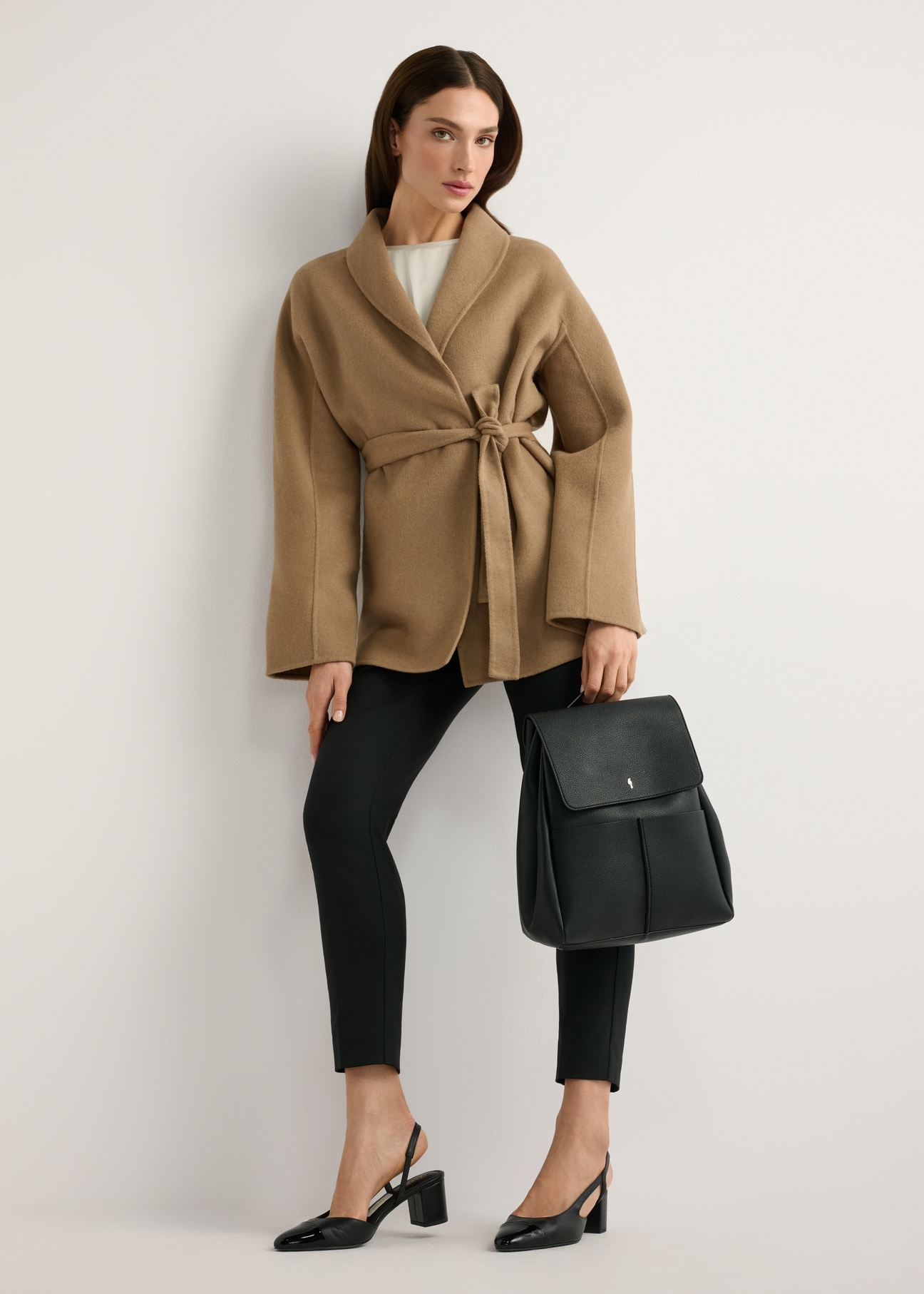 Czarny średni plecak damski TOREC-1132-99(W26) - widok produktu   z przodu, trzymanego przez modelkę w ręku, na jasnym tle. Widoczna cała sylwetka. 