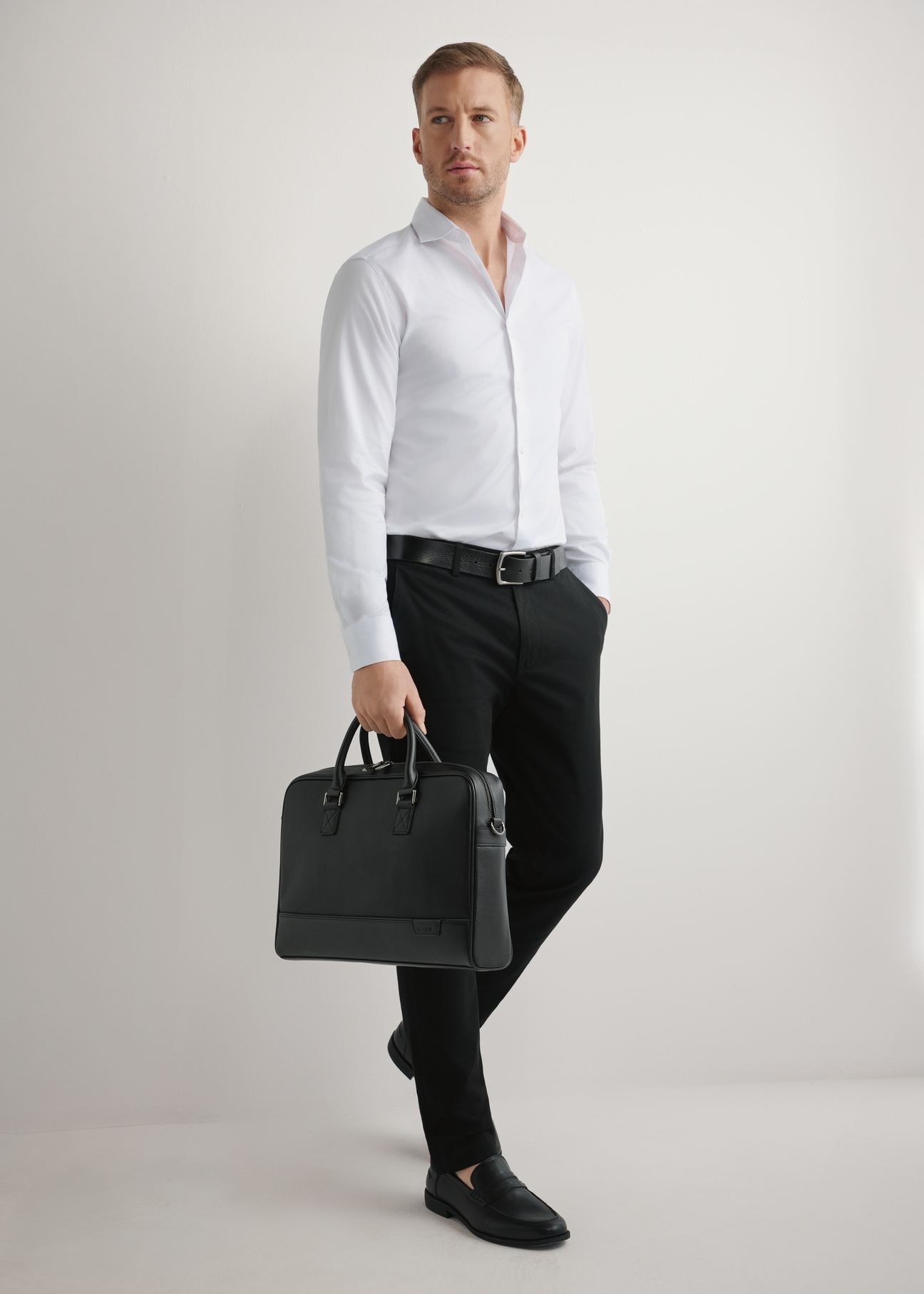 Czarna skórzana torba na laptopa TORMS-0494-99(W26) - widok produktu lekko po skosie, trzymanego przez modela w ręku, na jasnym tle. 