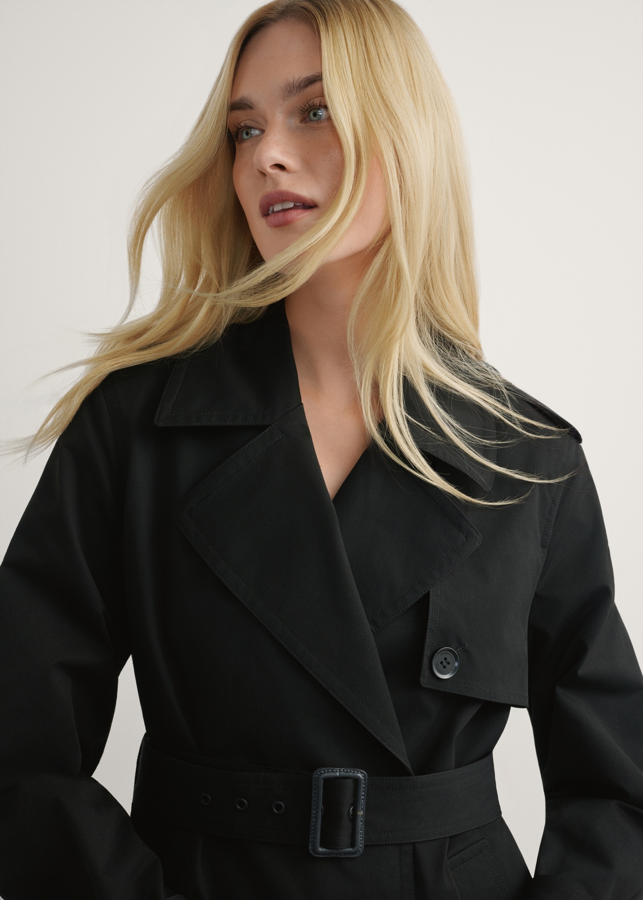 Długa czarna kurtka damska w formie płaszcza KURDT-0512-99(W25), widok produktu od przodu na modelce, widoczna połowa sylwetki.