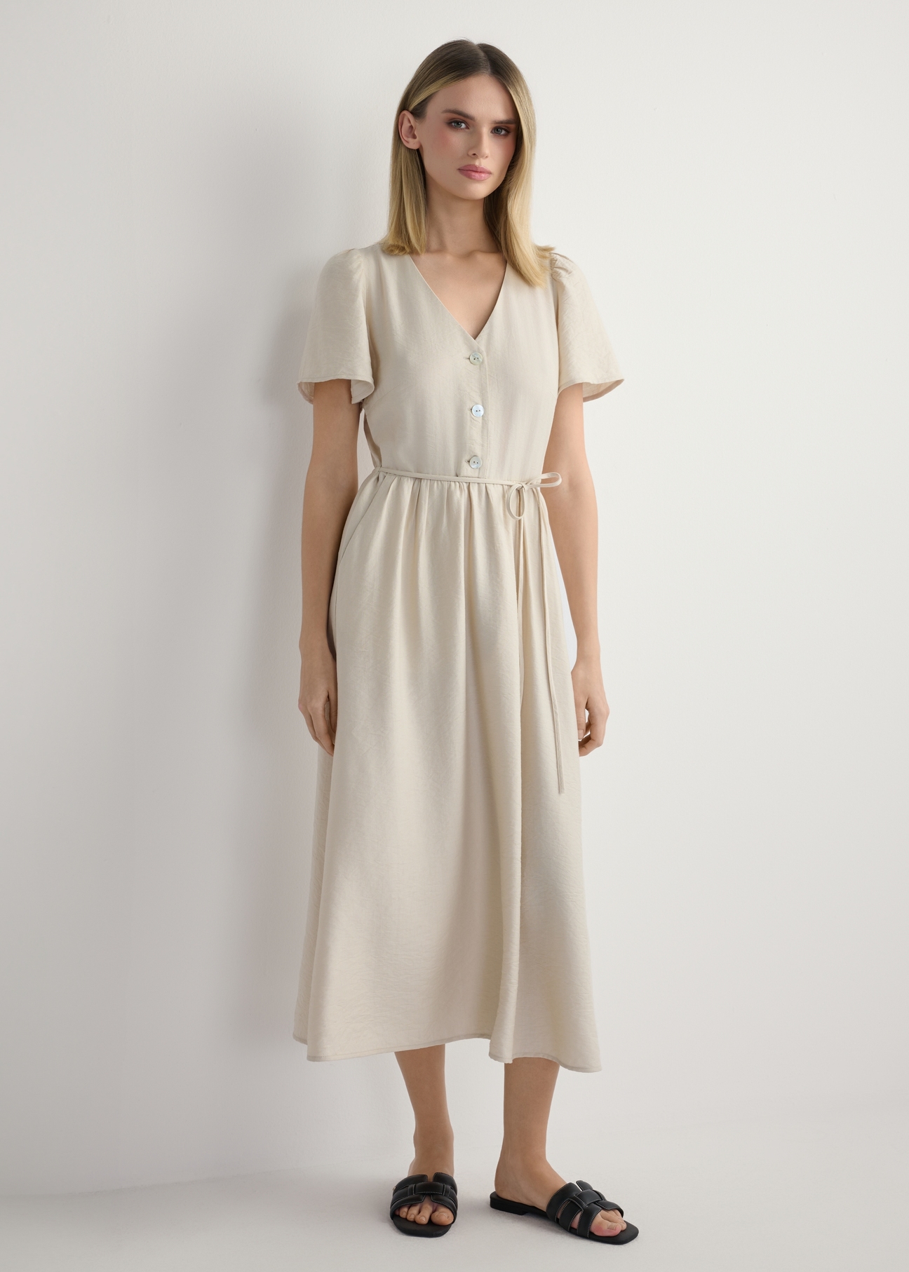 Sukienka damska w kolorze jasnego beżu SUKDT-0255-1A(W26), widok produktu z przodu na modelce. Widoczna cała sylwetka.