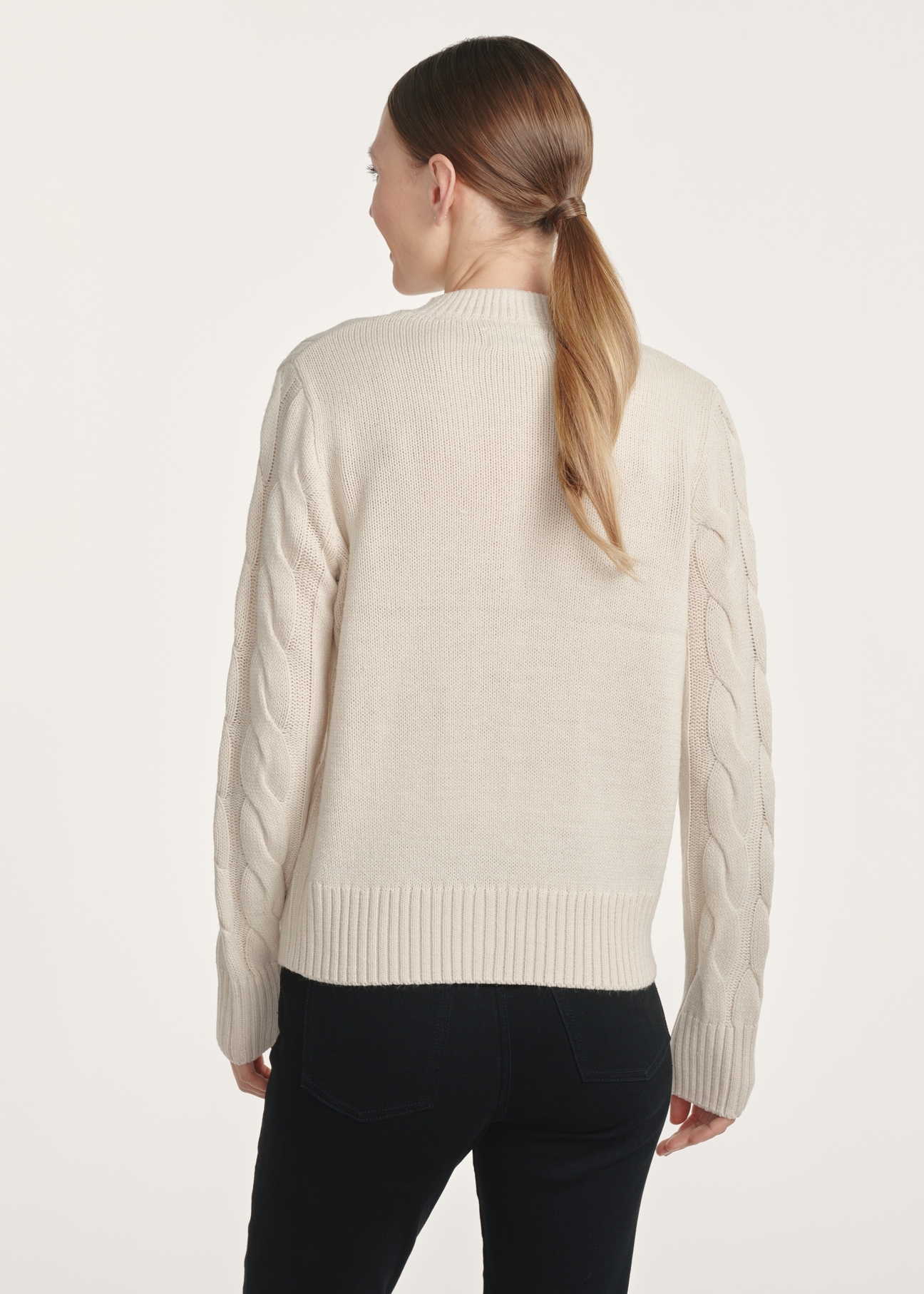 Jasnobeżowy sweter damski z ozdobnym splotem SWEDT-0210-80(Z25), widok produktu z tyłu na modelce. Widoczna połowa sylwetki.