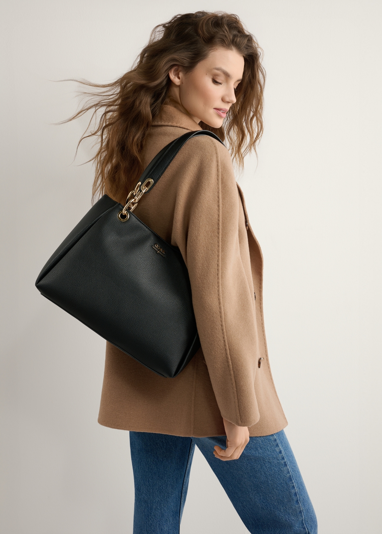 Czarna damska torebka z imitacji skóry TOREC-0998-99(W25), widok produktu od przodu na modelce, widoczna połowa sylwetki.