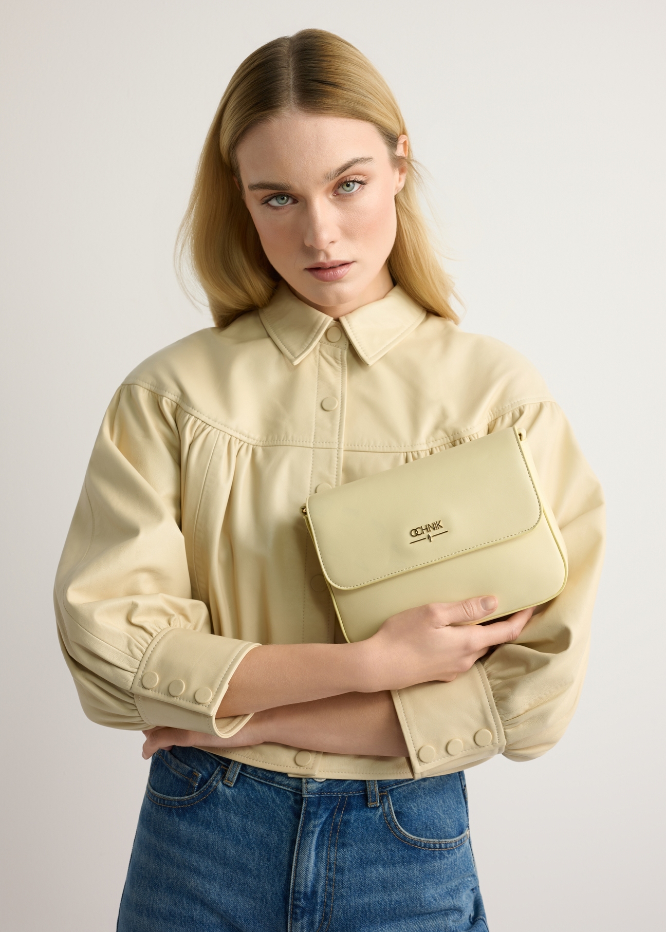 Jasnożółta listonoszka damska z łańcuszkiem TOREC-0767-2A(W26) - widok produktu z przodu, trzymanego przez modelkę w ręku, na jasnym tle. Widoczna połowa sylwetki. 