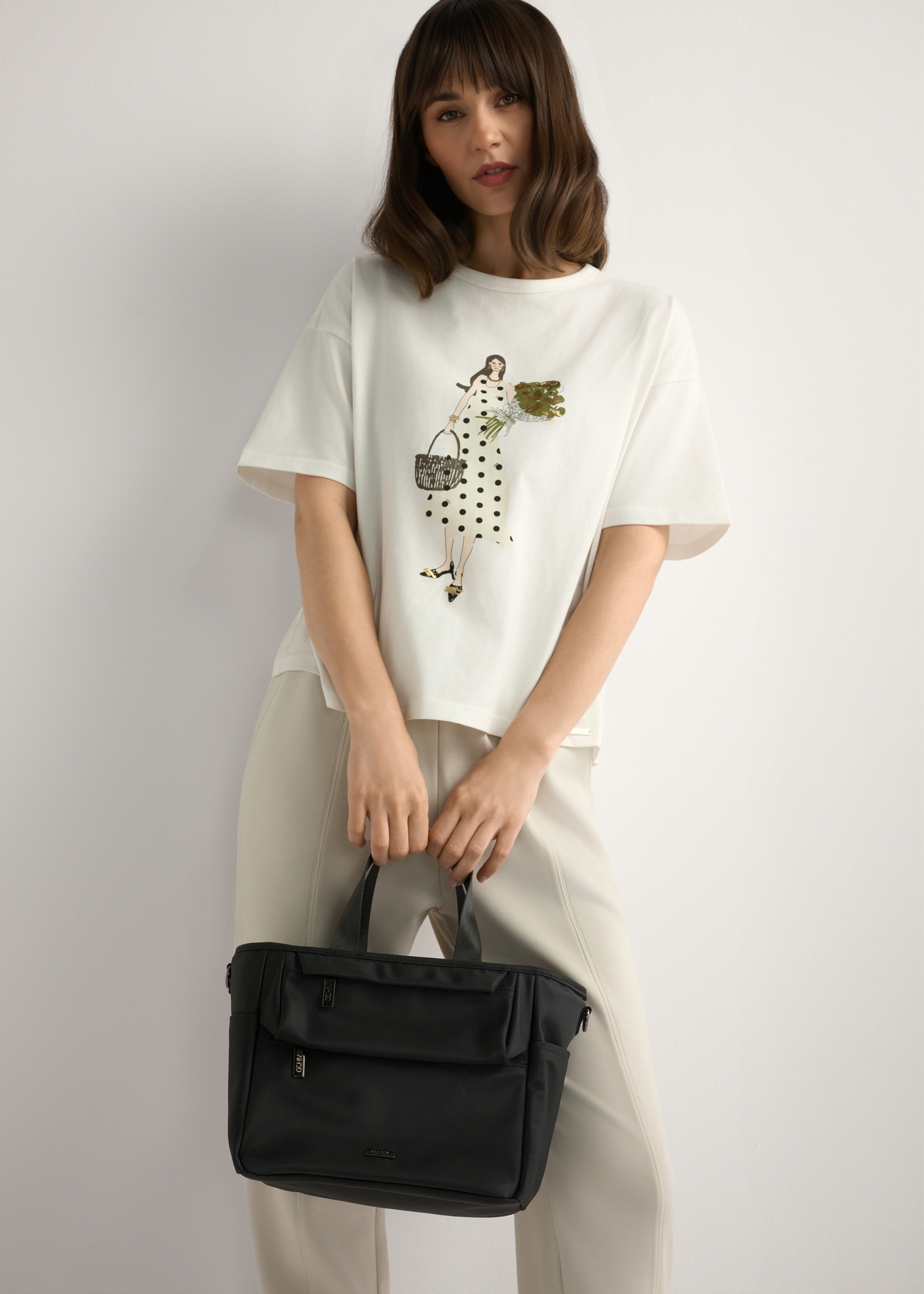 Czarna torebka typu lunchbox TOREN-0346-99(W26) - widok produktu trzymanego przez modelkę w ręku, na jasnym tle. Widoczna sylwetka do kolan.