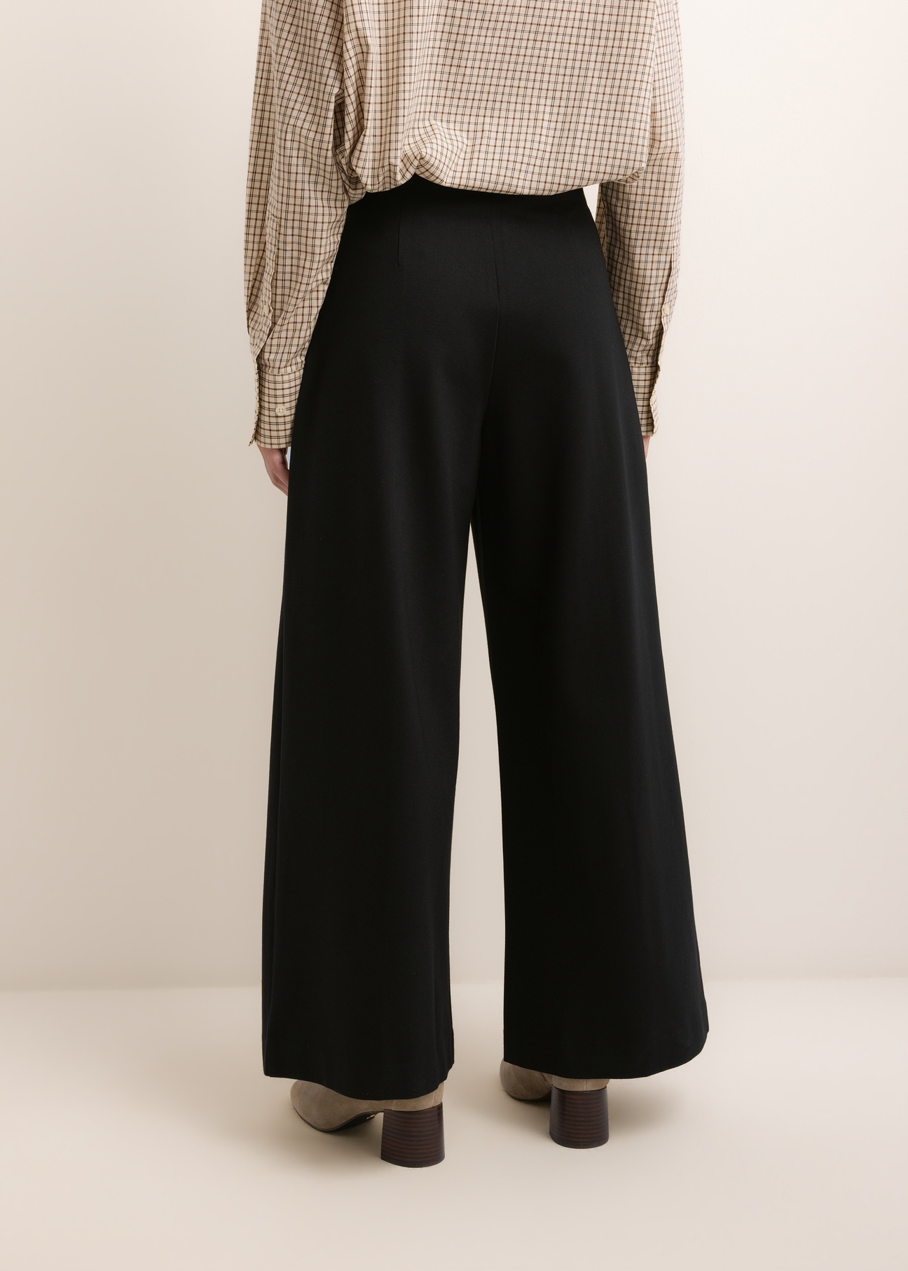 Czarne spodnie damskie wide leg SPODT-0130-99(Z26), widok produktu z tyłu na modelce. Widoczna połowa sylwetki.