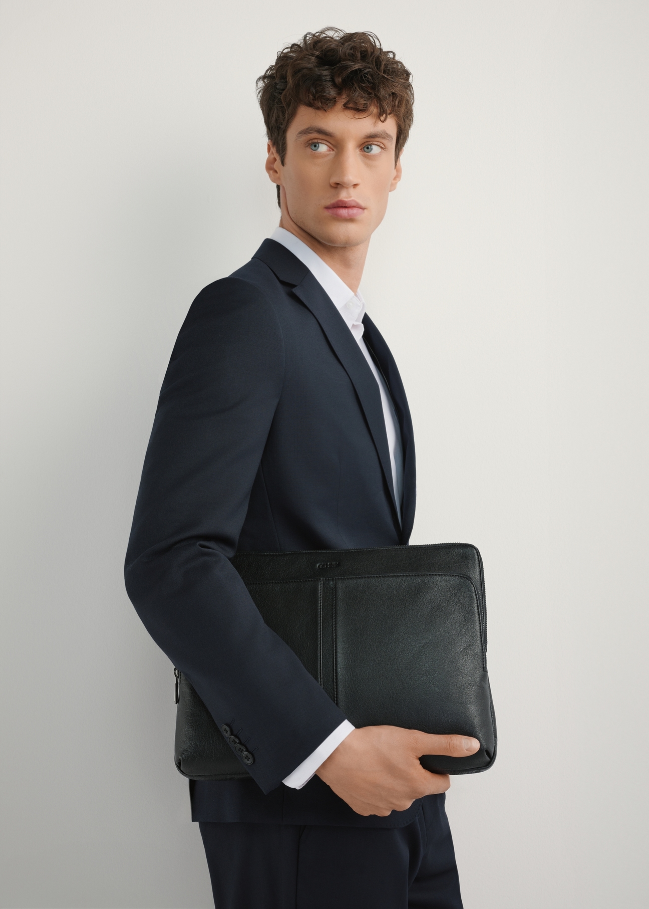 Czarna skórzana teczka na laptop TORMS-0455-99(W25), widok produktu od przodu na modelu, widoczna połowa sylwetki.