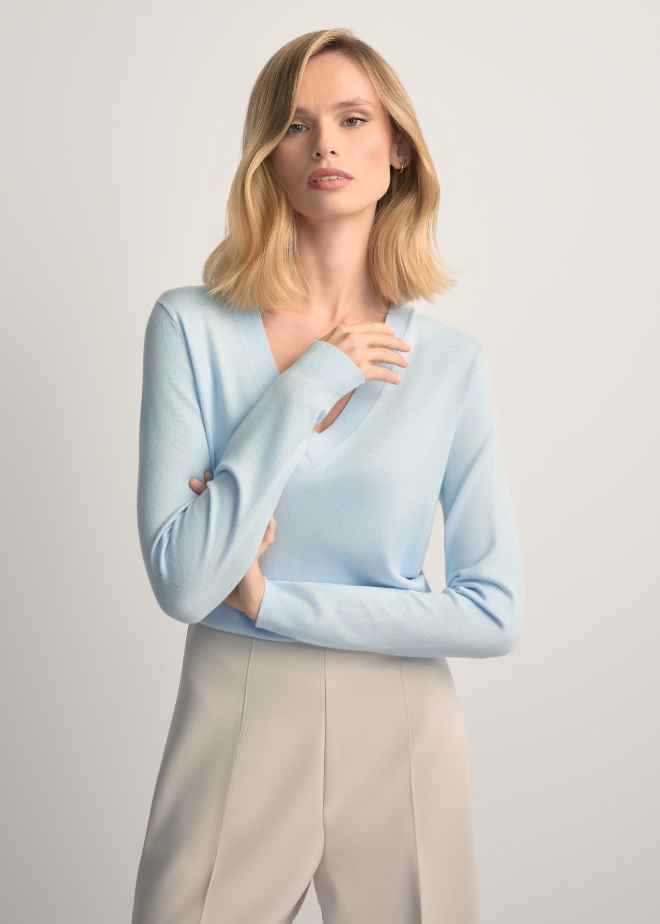 Jasnoniebieski sweter z dekoltem V-neck SWEDT-0201-7A(W26) - widok produktu z przodu, na modelce, na jasnym tle. Widoczna połowa sylwetki.