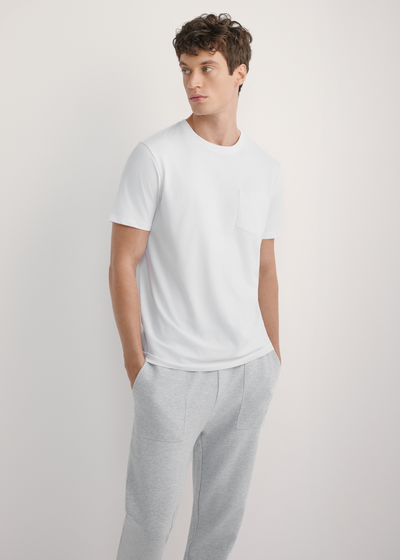 Biały T-shirt męski TSHMT-0137-0A(W26) - widok produktu z przodu, na modelu, na jasnym tle. Widoczna sylwetka do kolan. 