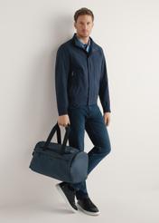 Granatowa torba podróżna TORMN-0412-7D(W26) - widok produktu, trzymanego przez modela w ręku, na jasnym tle. Widoczna cała sylwetka. 