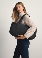 Czarna torebka shopper damska TOREN-0336-99(W26) - widok produktu z boku, na modelce, na jasnym tle. Widoczna połowa sylwetki.