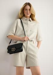 Czarna torebka listonoszka damska TOREC-1120-99(W26) - widok produktu lekko po skosie, na modelce, na jasnym tle. Widoczna sylwetka do kolan.