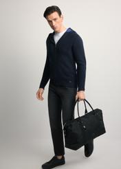 Czarna torba podróżna TORMN-0382-99(Z25) - widok produktu po skosie, trzymanego przez modela w ręku, na jasnym tle. Widoczna cała sylwetka.  