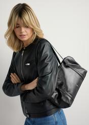 Czarna torebka damska z połyskiem TOREC-1205-9F(W26) - widok produktu lekko po skosie, na modelce, na jasnym tle. Widoczna połowa sylwetki. 