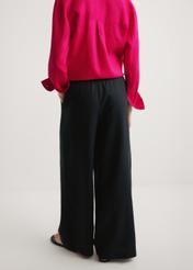 Czarne lniane spodnie damskie SPODT-0124-99(W26) - widok produktu z tyłu, na modelce, na jasnym tle. Widoczna połowa sylwetki. 