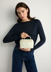 Kremowa kosmetyczka damska TOREC-1197-0A(W26) - widok produktu z przodu, trzymanego przez modelkę w ręku, na jasnym tle. Widoczna sylwetka do połowy. 